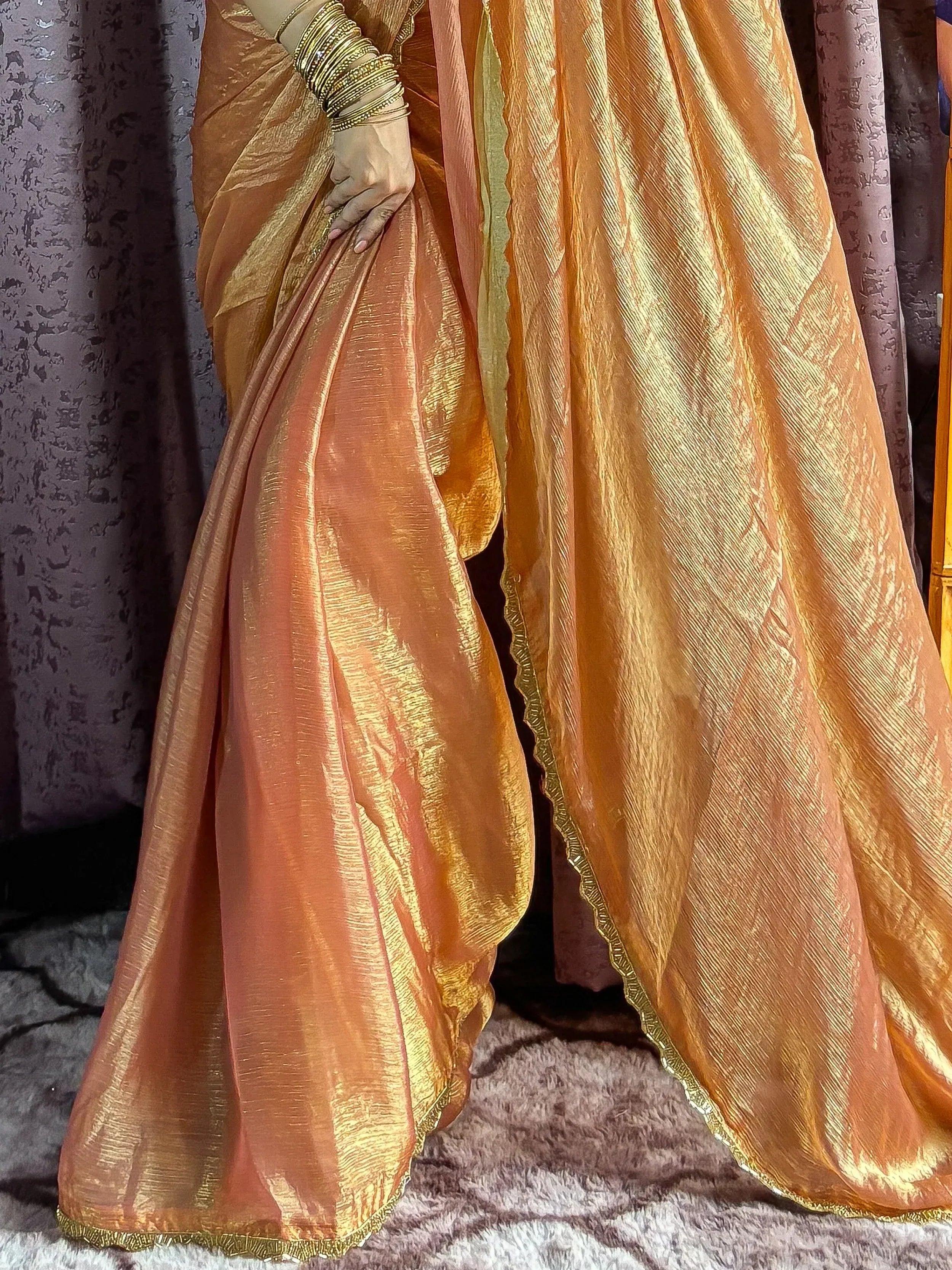 Golden orange saree with shimmering texture and scalloped border, styled with traditional bangles