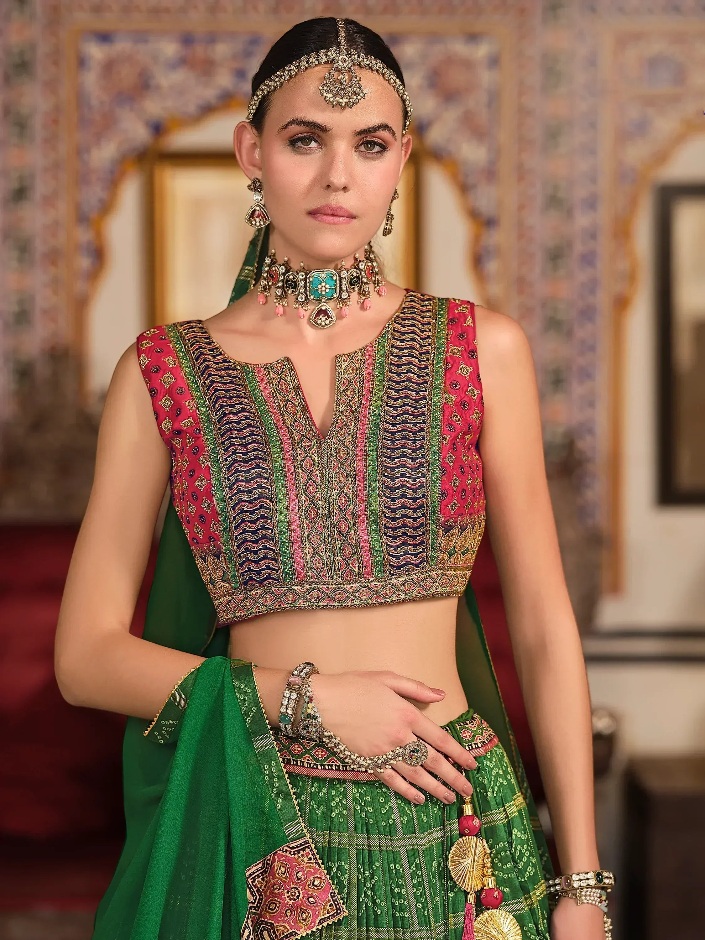 Woman in vibrant green and pink embroidered lehenga choli with traditional Indian jewelry