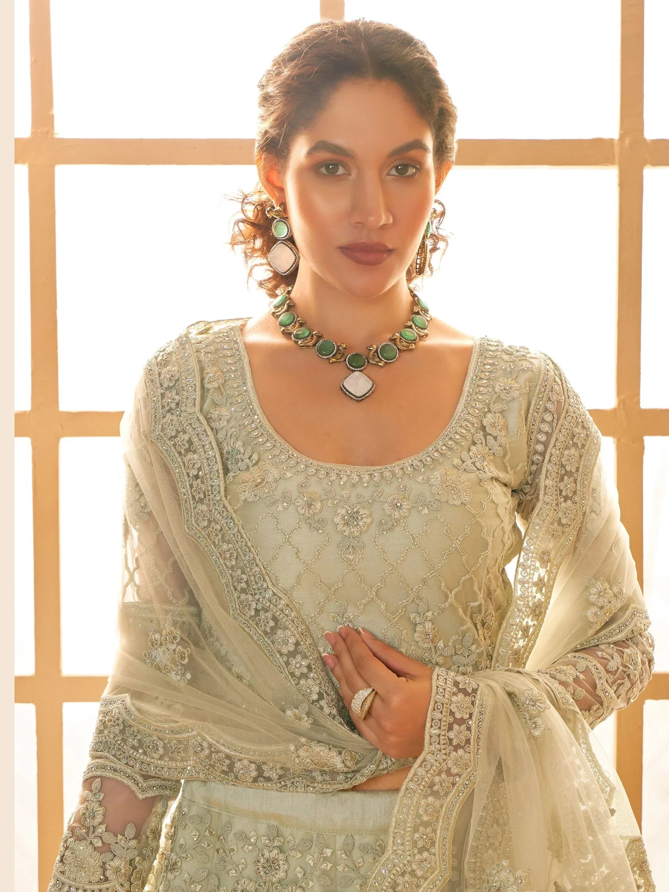 Elegant Indian ethnic wear with intricate embroidery and green stone jewelry, perfect for festive occasions.