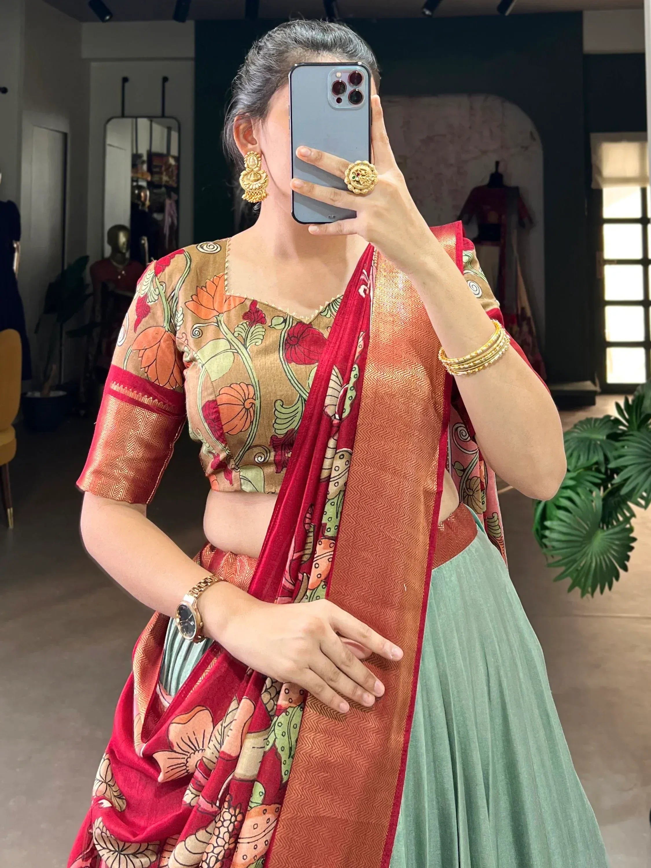Woman in floral print lehenga choli with red dupatta, gold jewelry, taking mirror selfie
