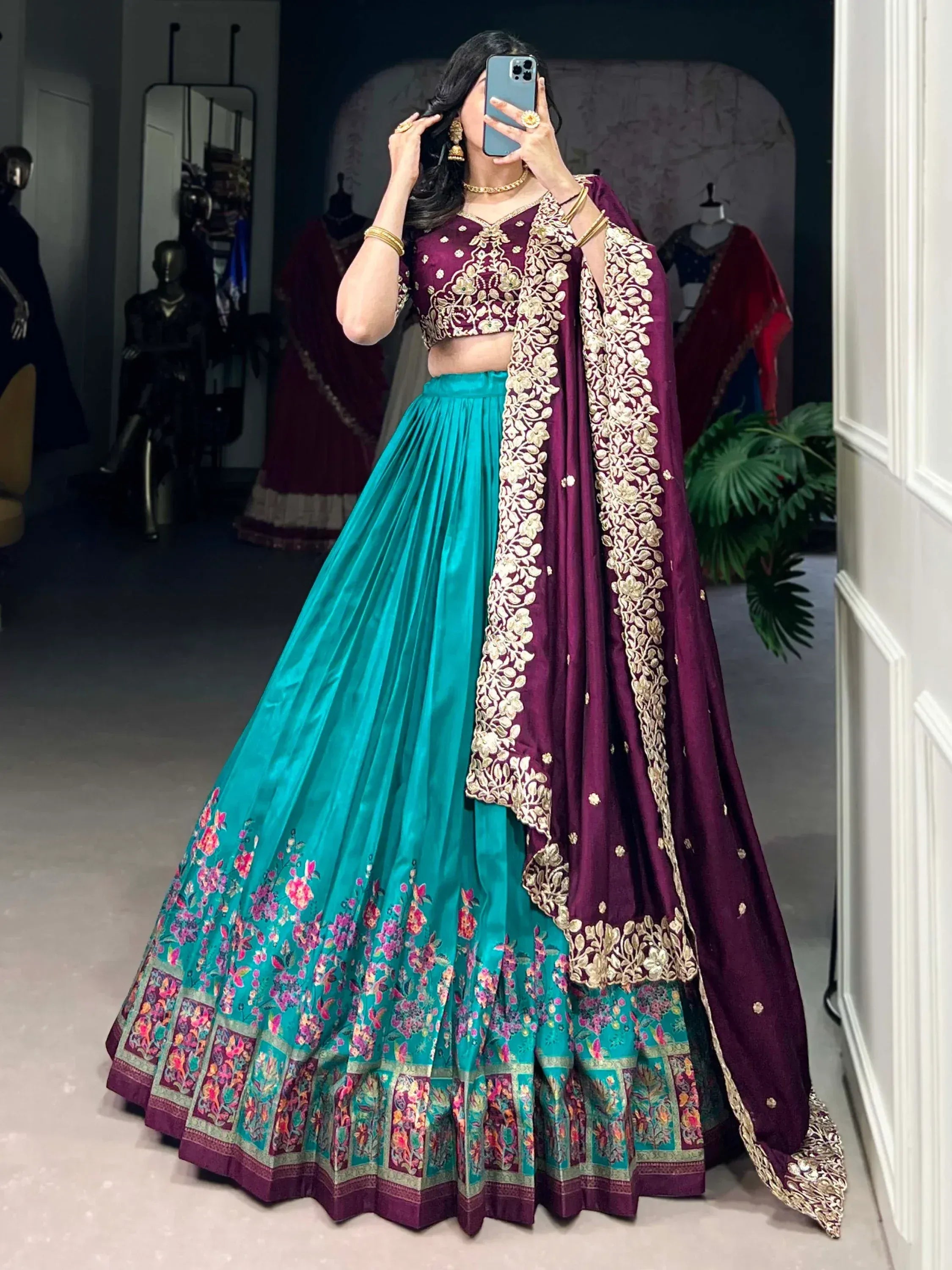 Woman in maroon and teal designer lehenga choli with gold embroidery, perfect for Indian weddings and festivals.