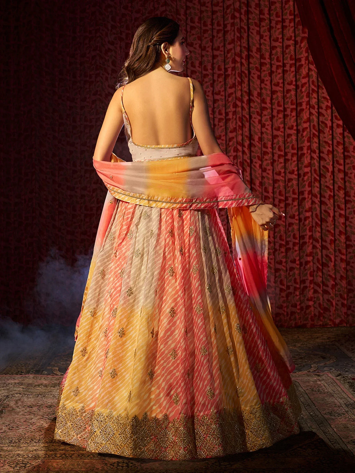 Woman in backless designer lehenga choli with ombre pink yellow skirt, gold embroidery, perfect for Indian ethnic wear events