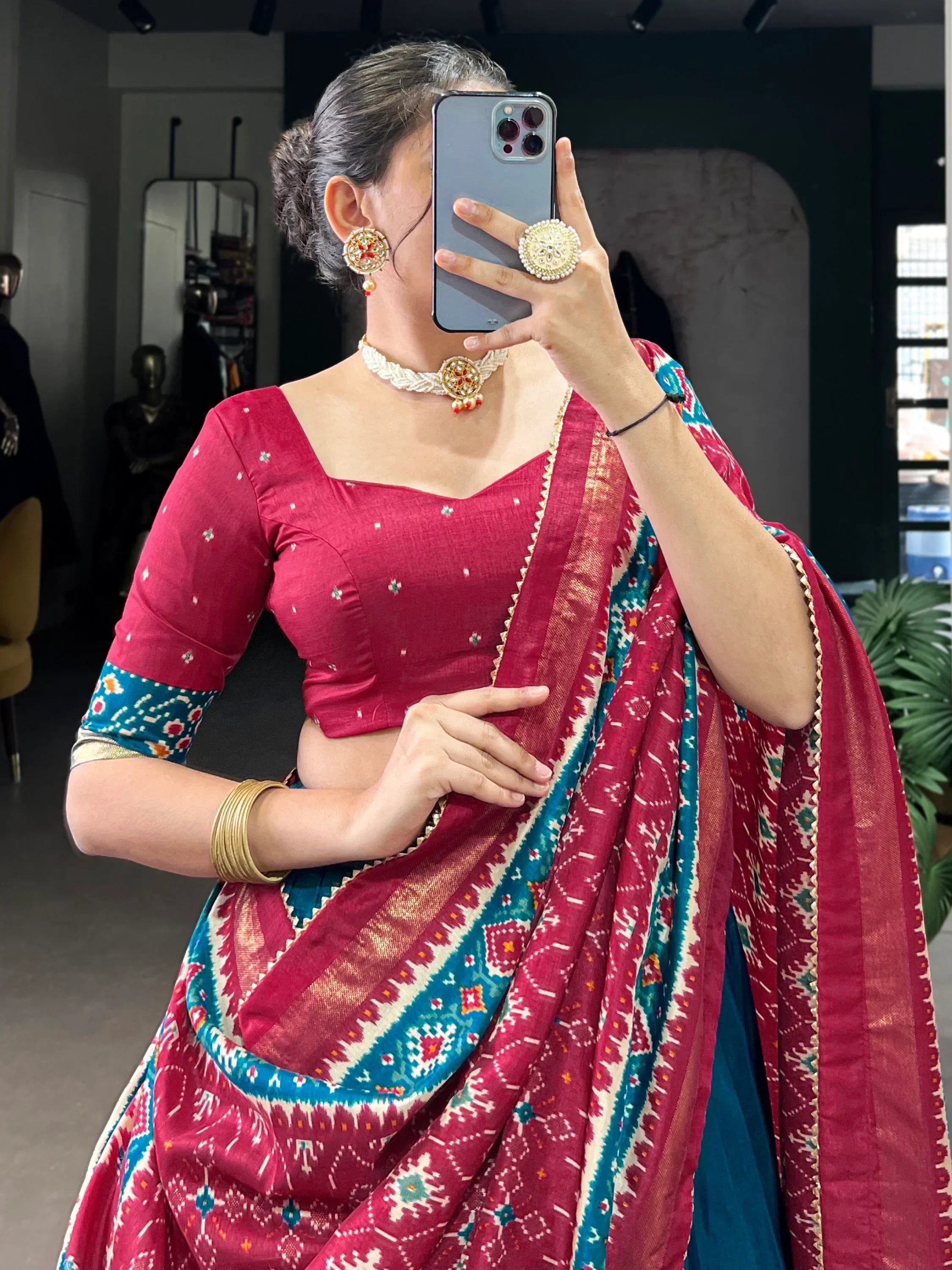 Woman in red and teal ethnic saree with mirror work blouse, traditional jewelry, taking mirror selfie
