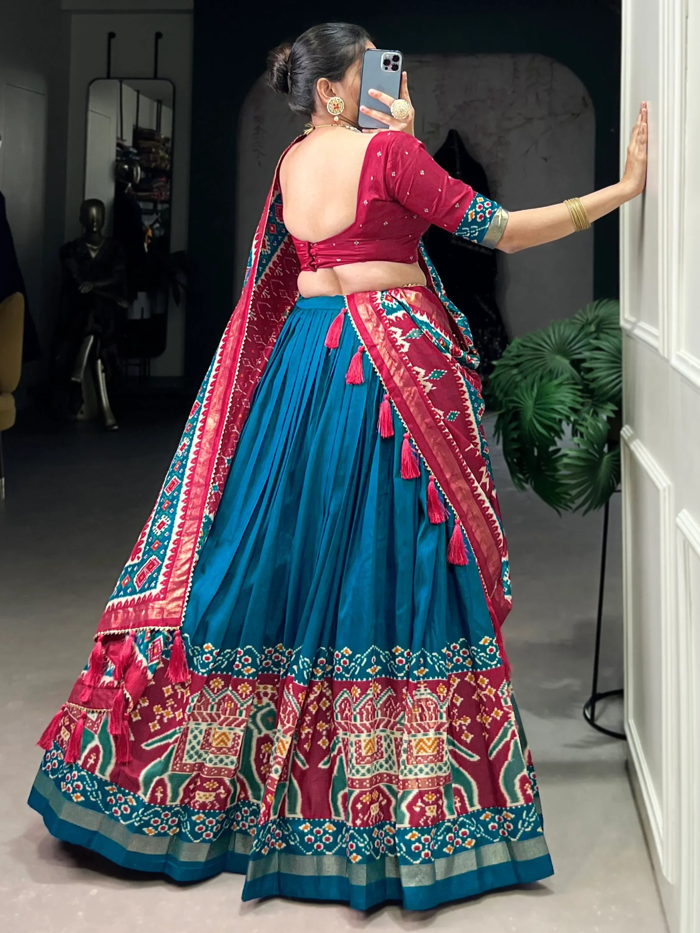 Woman in vibrant blue and red ethnic lehenga choli with mirror work, tassels, and traditional print, taking mirror selfie