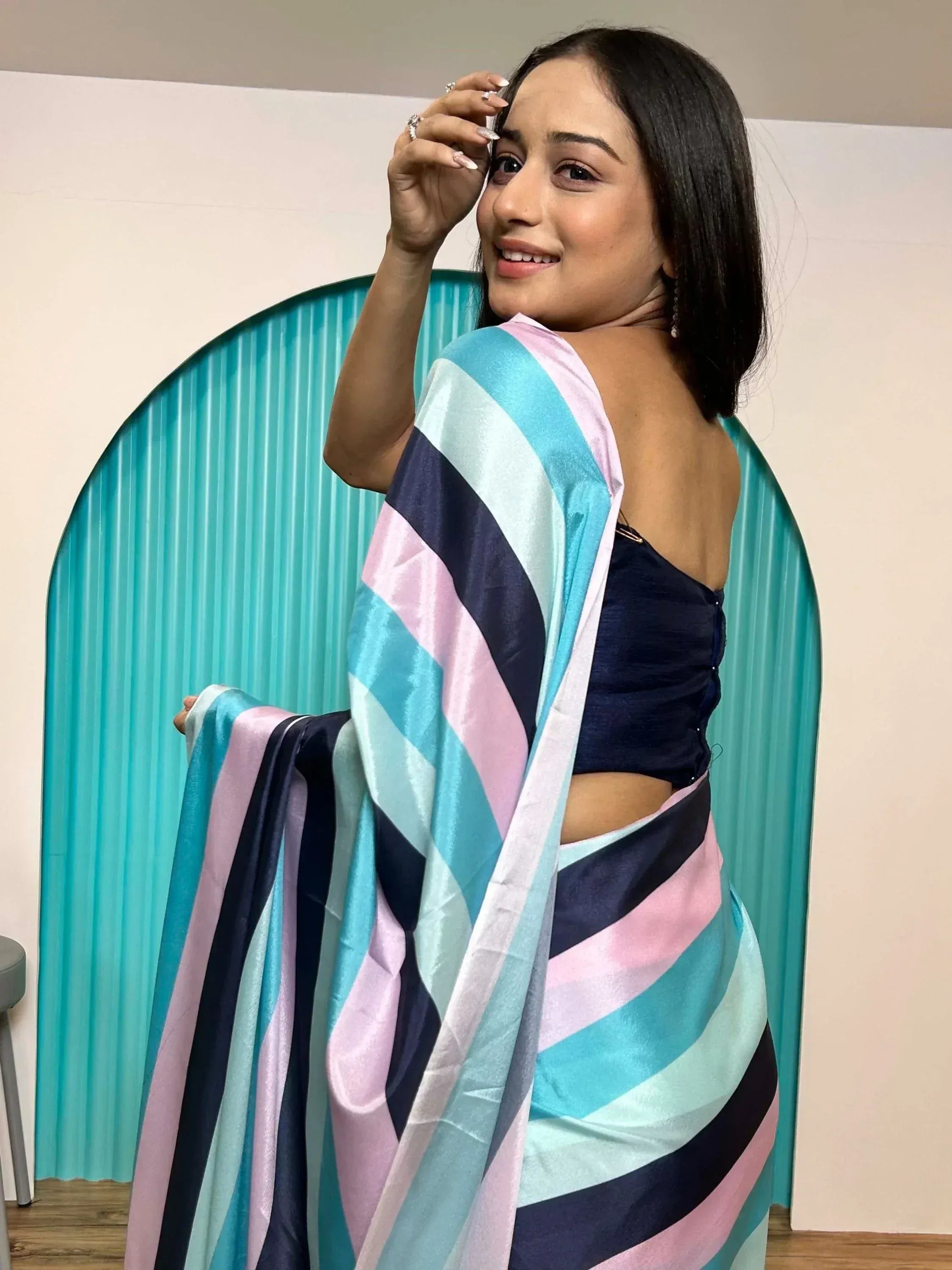 Woman in striped saree with blue, pink, and navy hues, paired with a black blouse, posing elegantly.