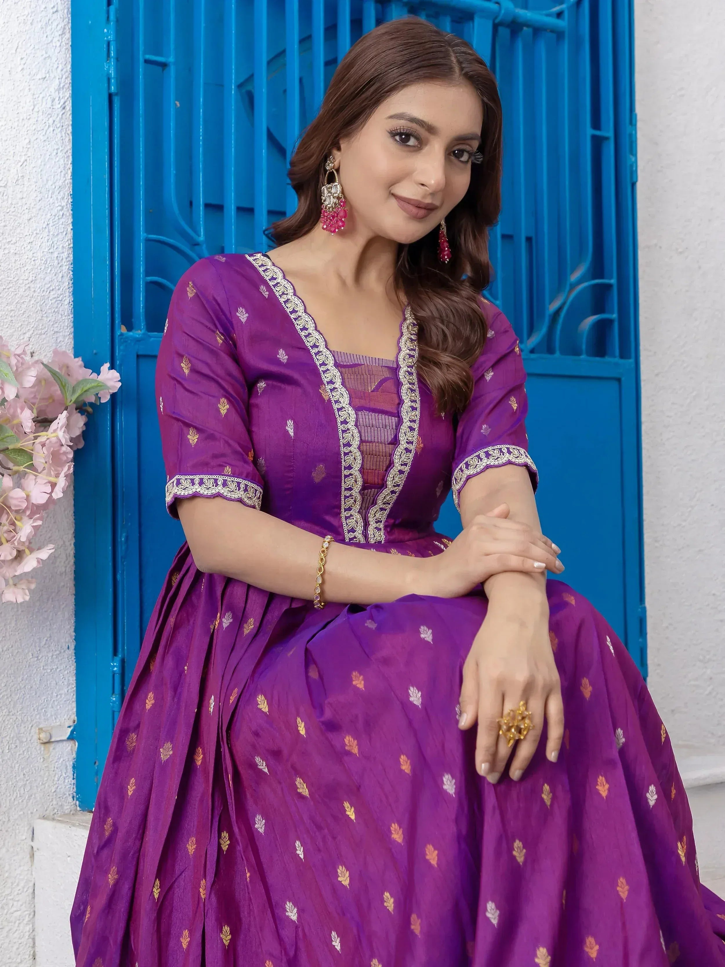Purple ethnic gown with gold embroidery, styled with statement earrings and a blue door backdrop