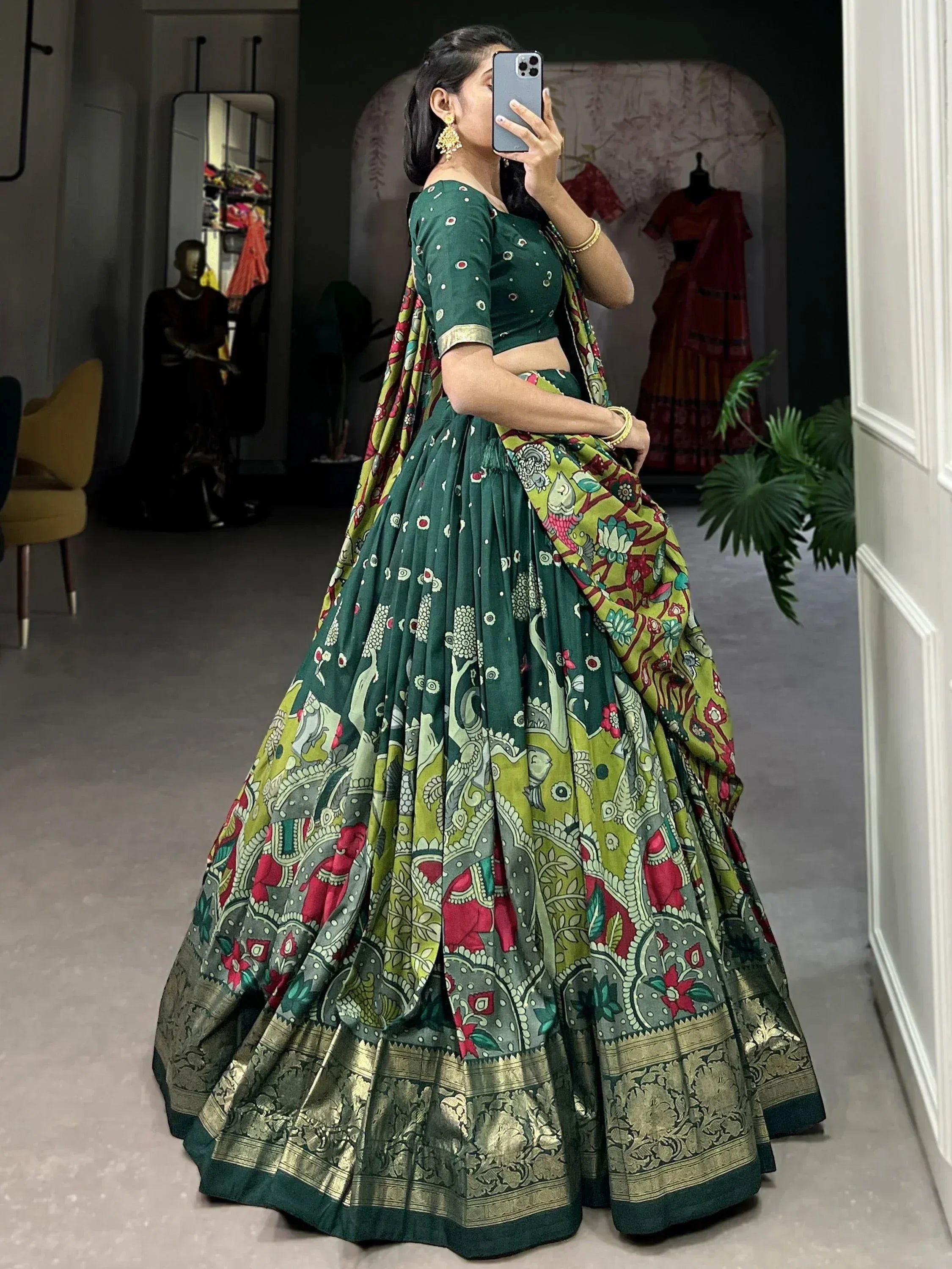 Woman in green printed lehenga choli with floral and elephant motifs, taking mirror selfie in boutique