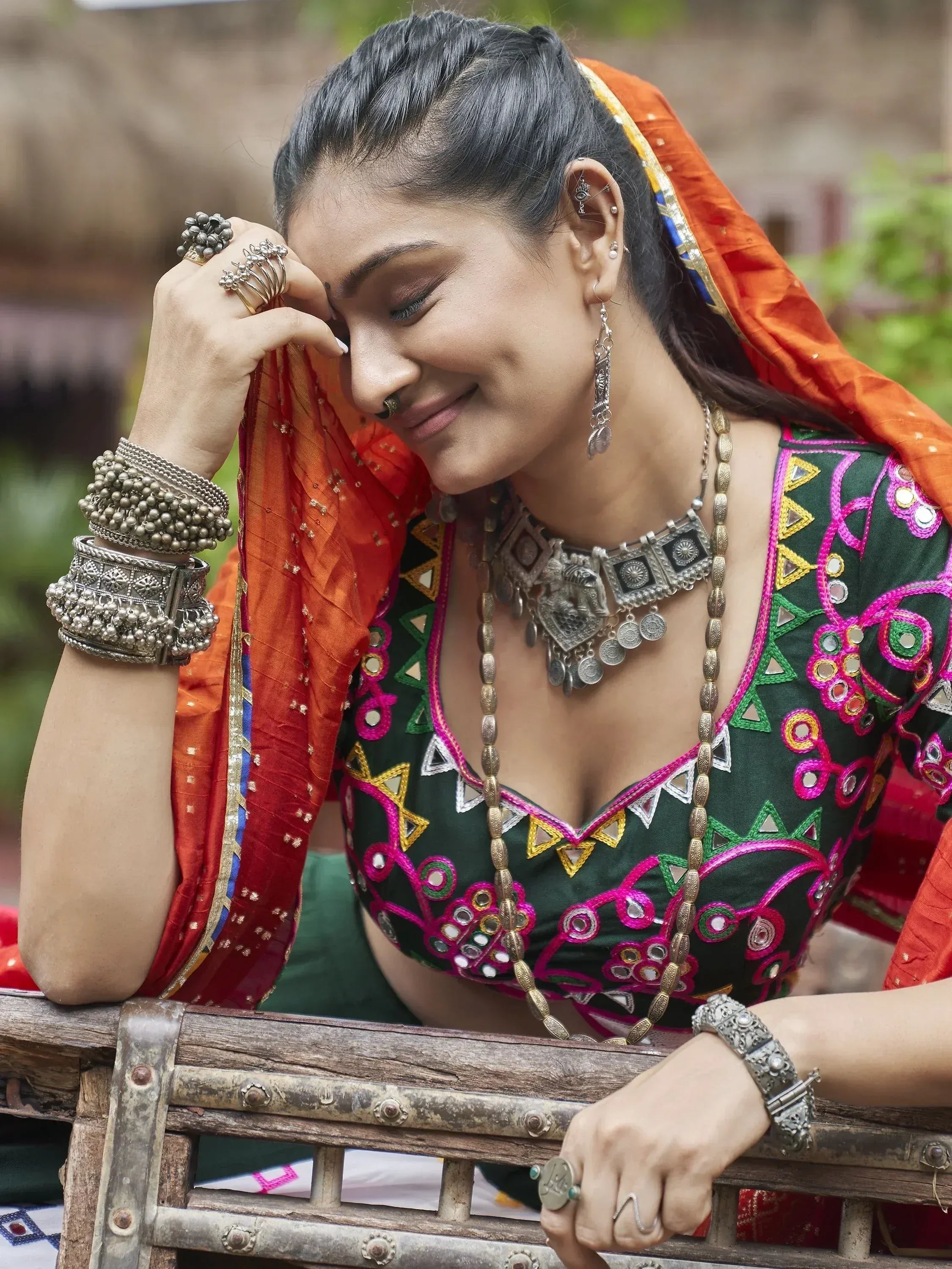 Woman in vibrant green embroidered choli with orange dupatta, traditional silver jewelry, and mirror work, styled for Indian ethnic wear.