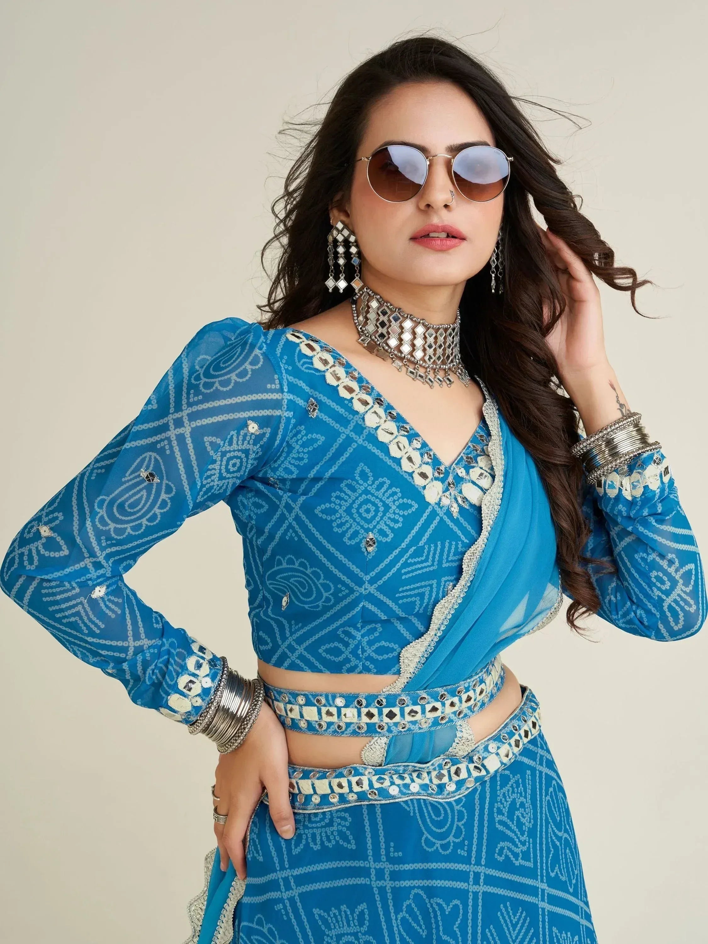 Blue mirror work lehenga choli with ethnic print, statement jewelry, and sunglasses for festive Indian wear