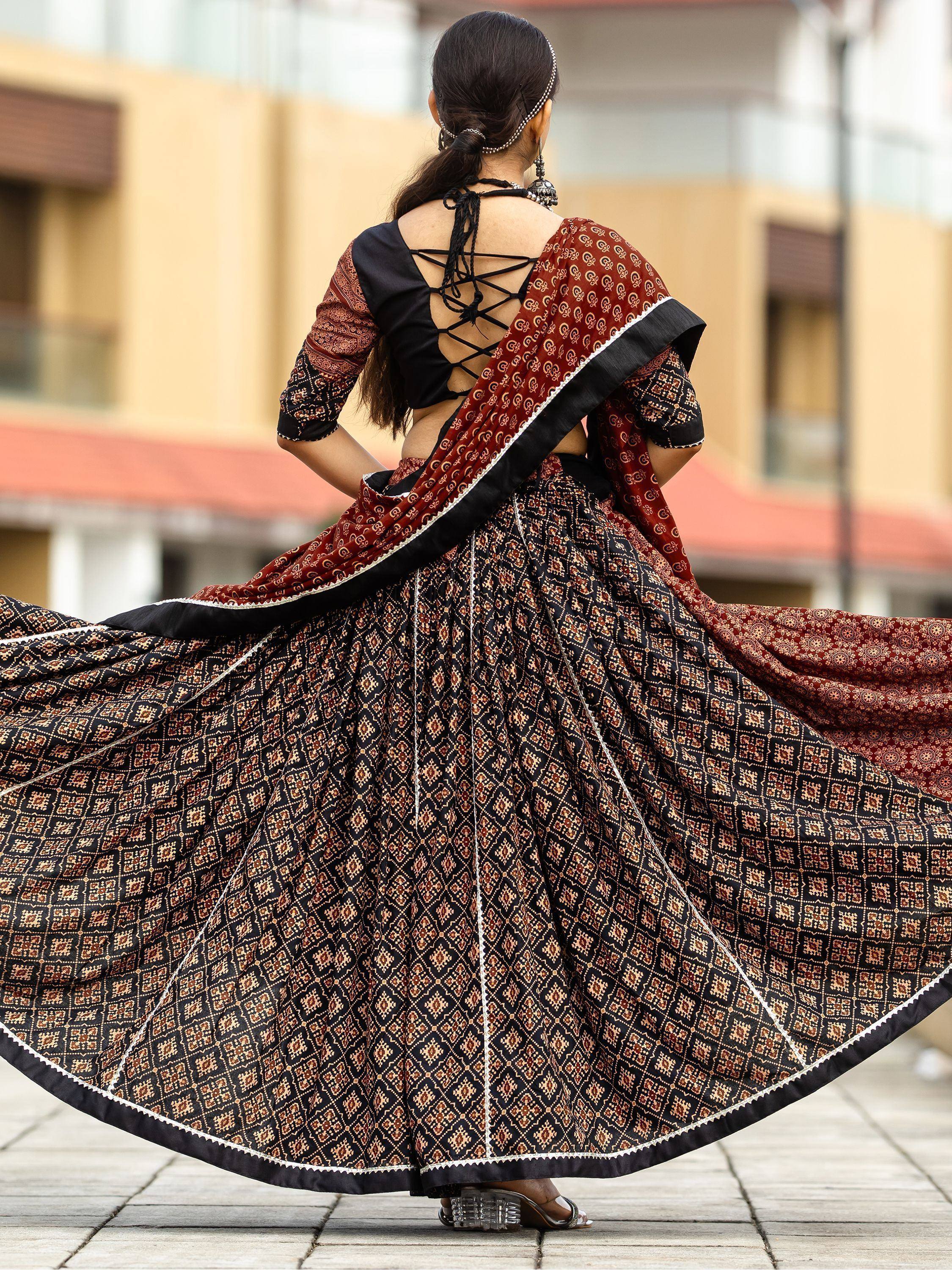 Woman twirling in black and maroon printed lehenga choli with lace-up back, showcasing ethnic Indian wear.