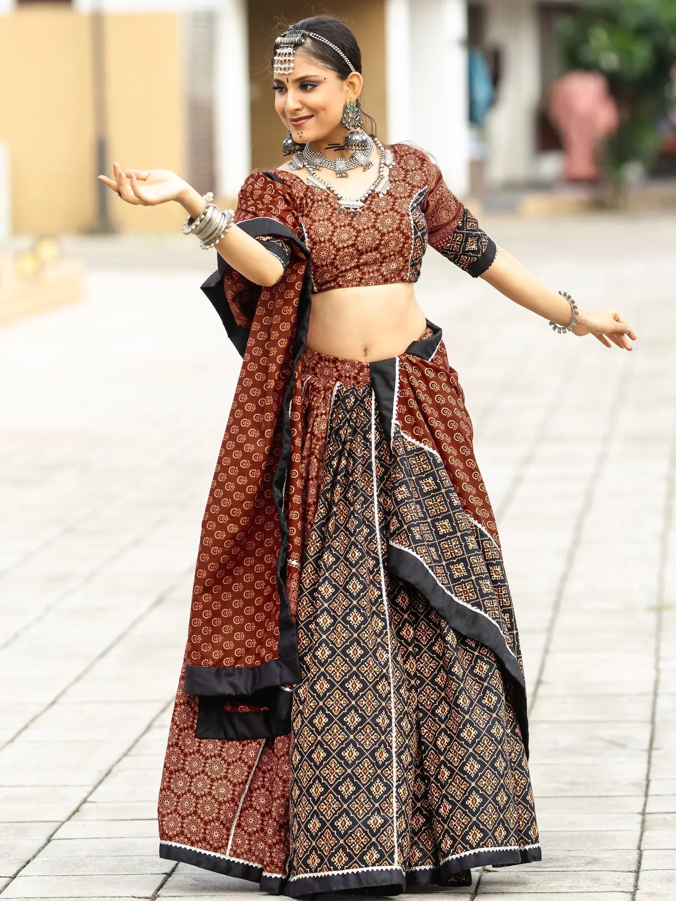 Woman in maroon and black printed lehenga choli with traditional jewelry, dancing outdoors