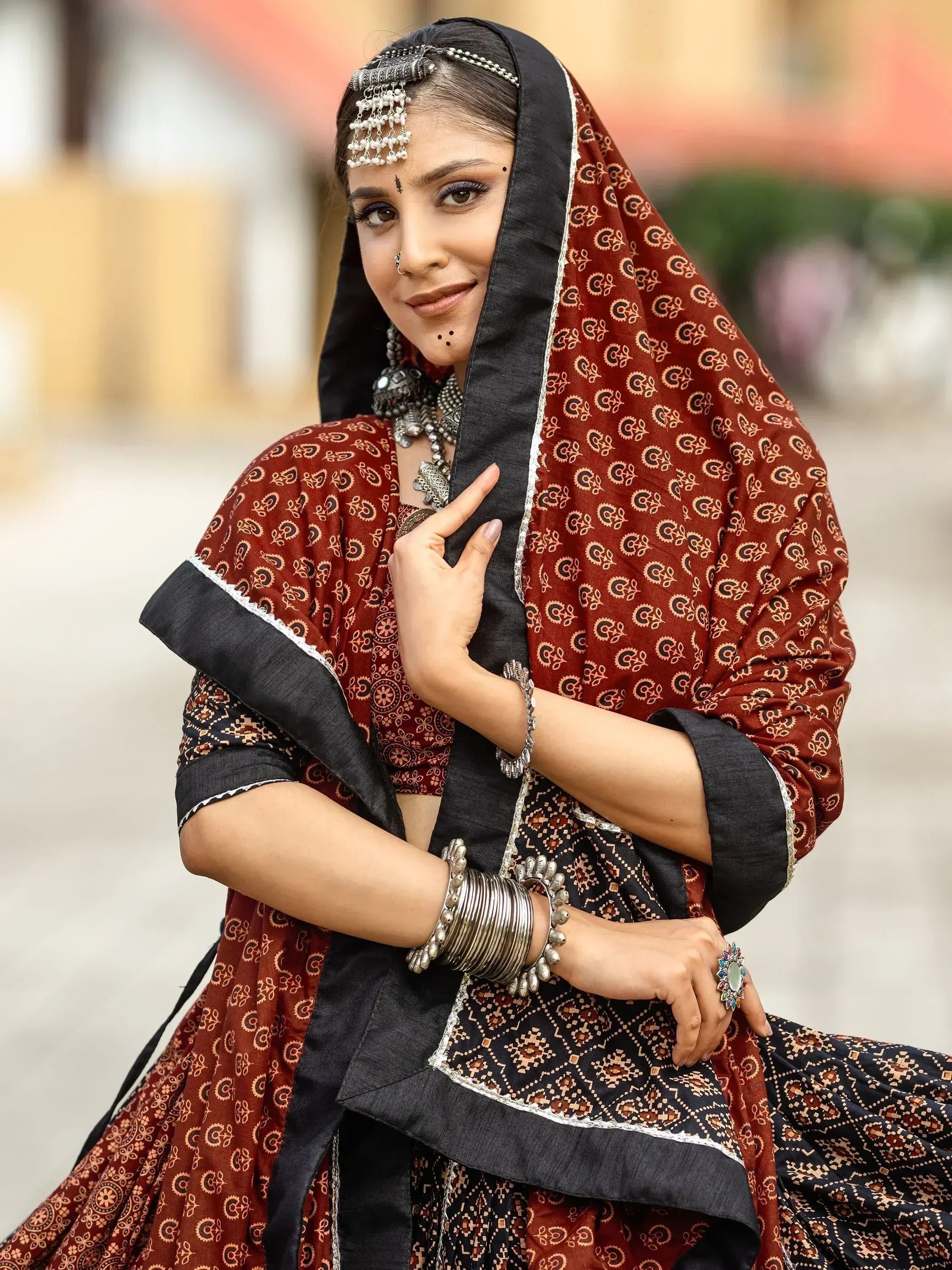 Woman in traditional Indian ethnic wear with red and black printed lehenga choli, silver jewelry, and dupatta