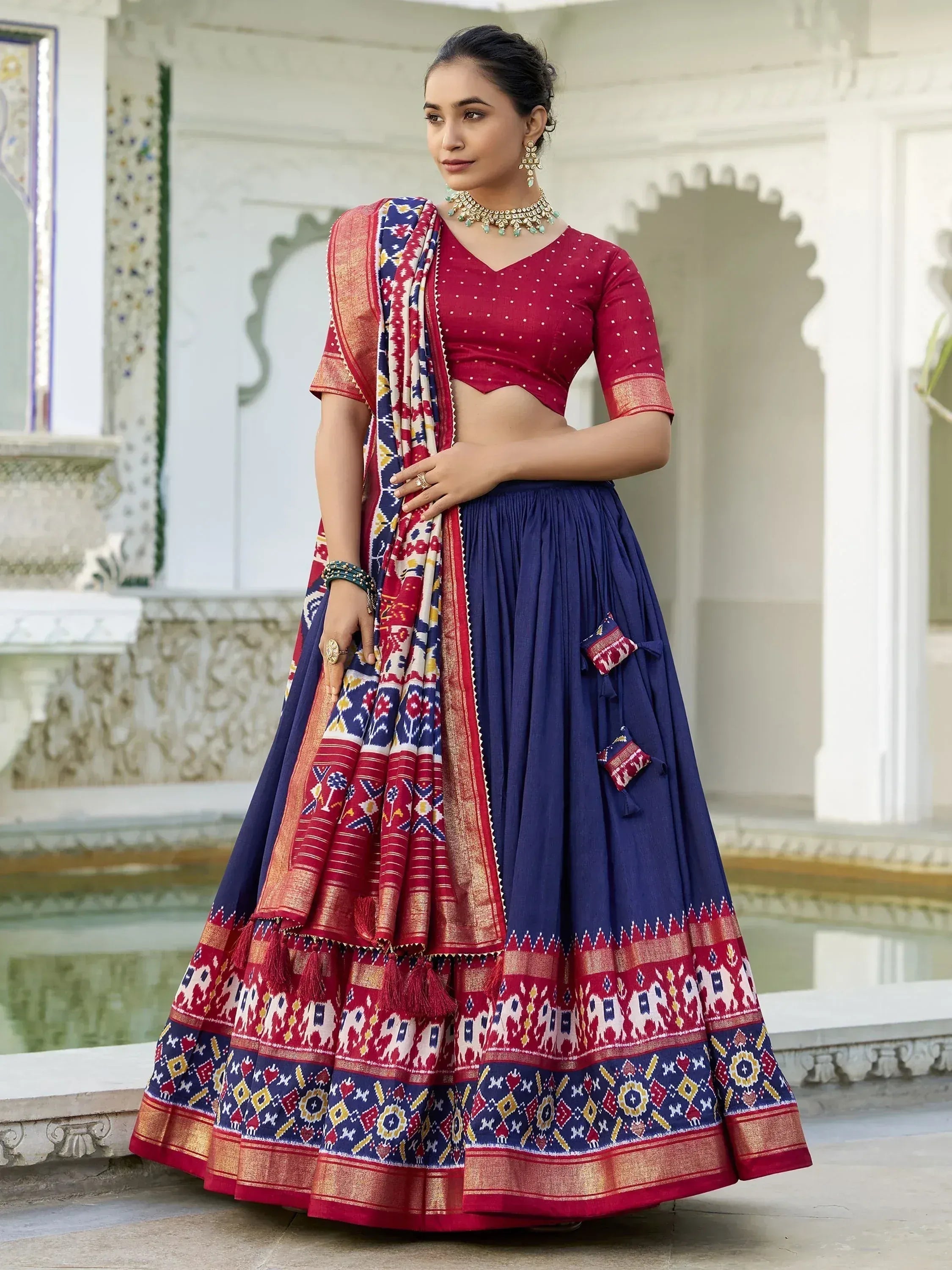 Woman in red and blue ethnic lehenga choli with ikat print, perfect for Indian weddings and festivals.