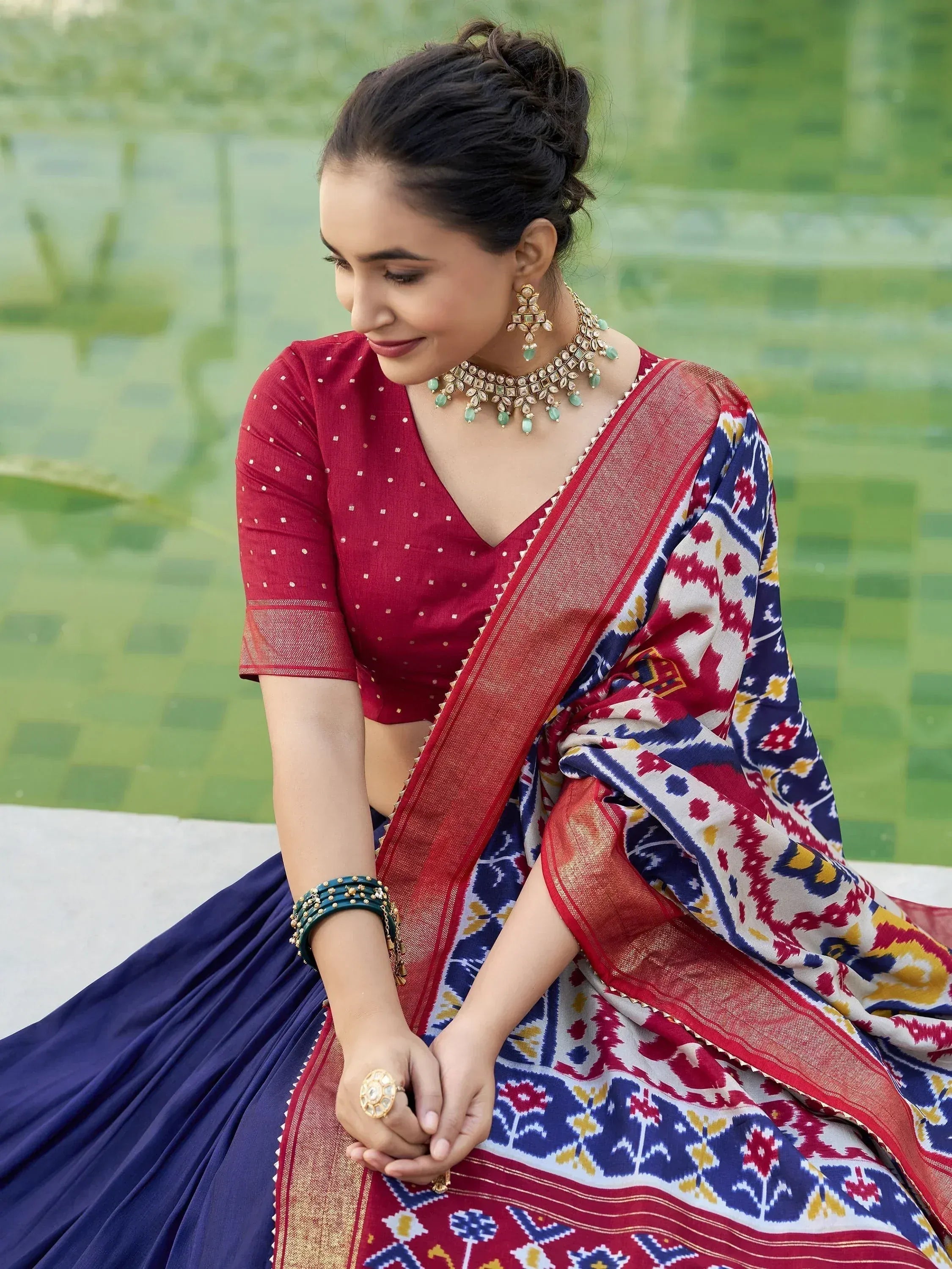 Woman in vibrant Indian saree with ikat print, red blouse, and traditional jewelry, perfect for ethnic occasions.