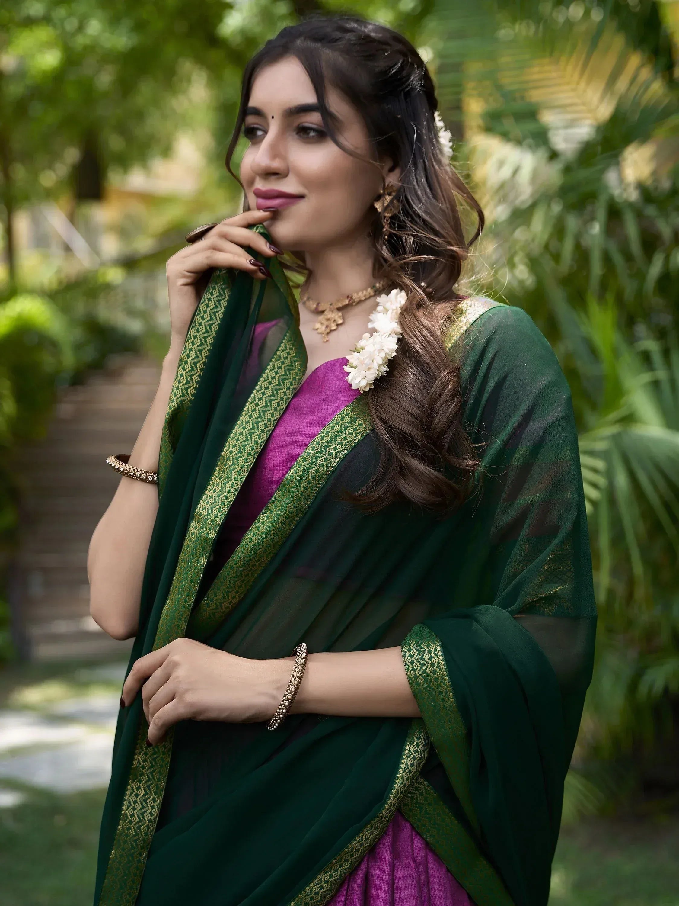 Woman in green and purple ethnic saree with gold border, floral hair accessory, garden setting