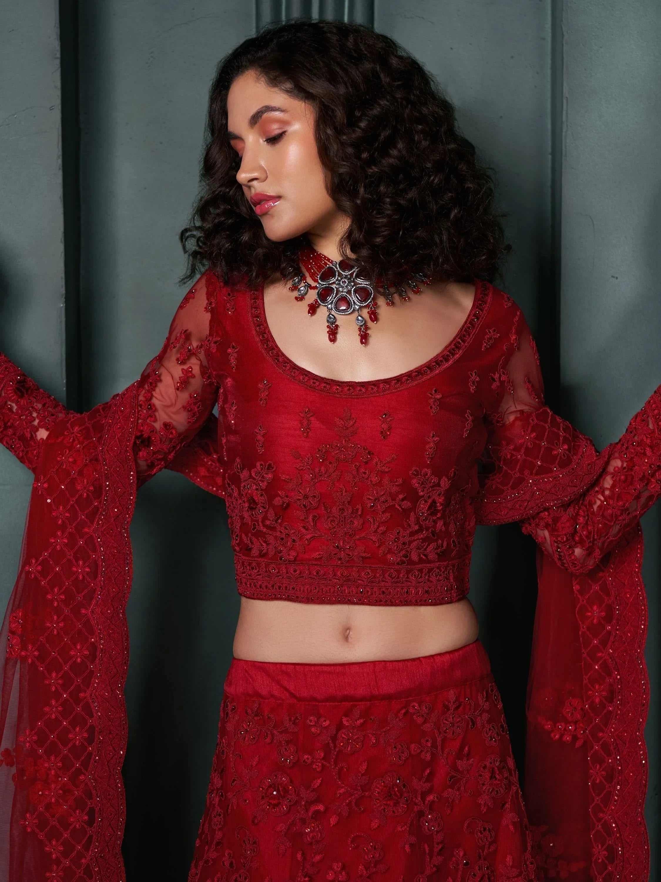 Red embroidered lehenga choli with sheer sleeves and matching jewelry for Indian ethnic wear