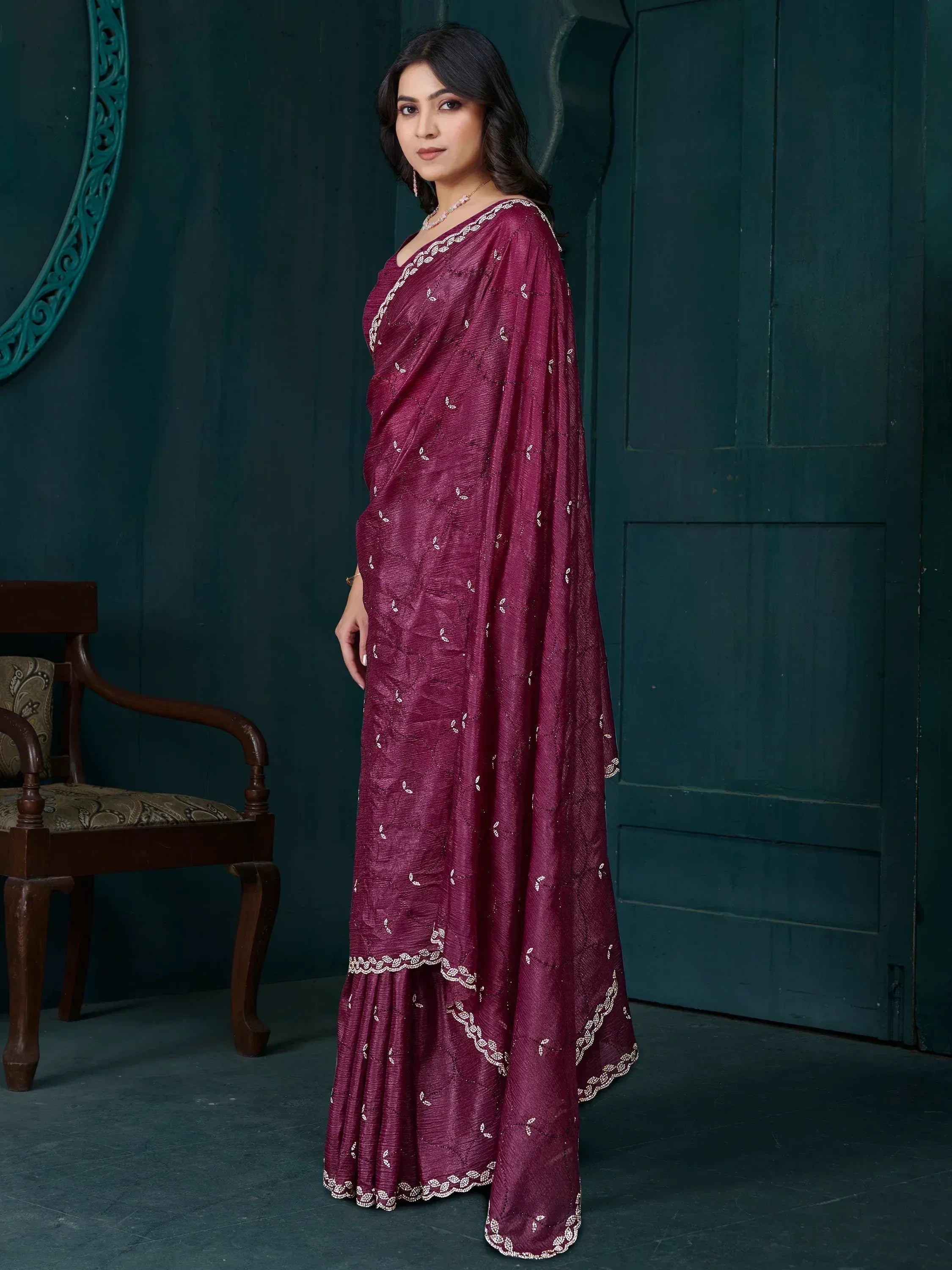 Woman in maroon ethnic saree with white embroidery, standing against dark teal door