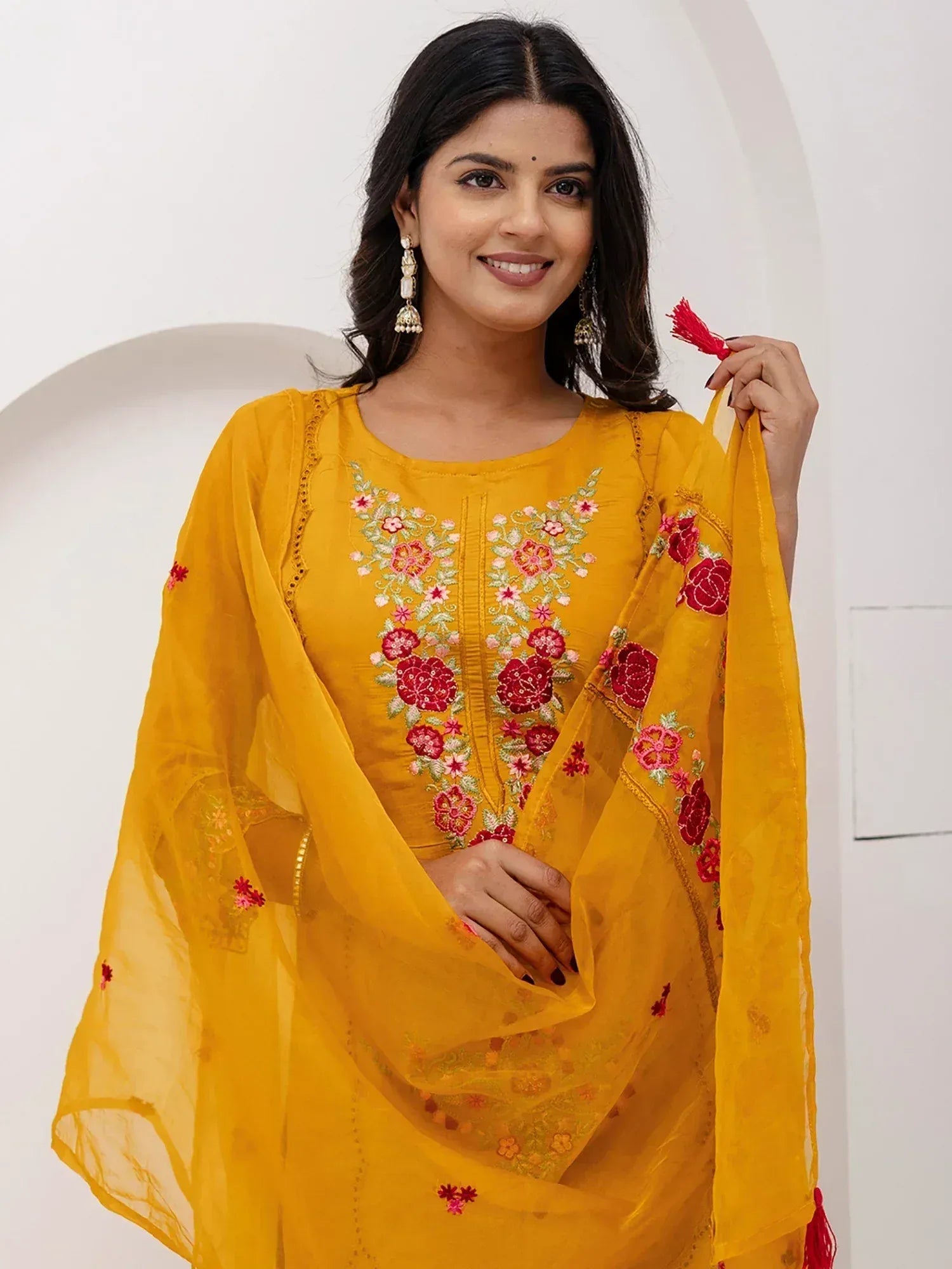 Yellow embroidered salwar kameez with floral design and red tassels, perfect for ethnic occasions