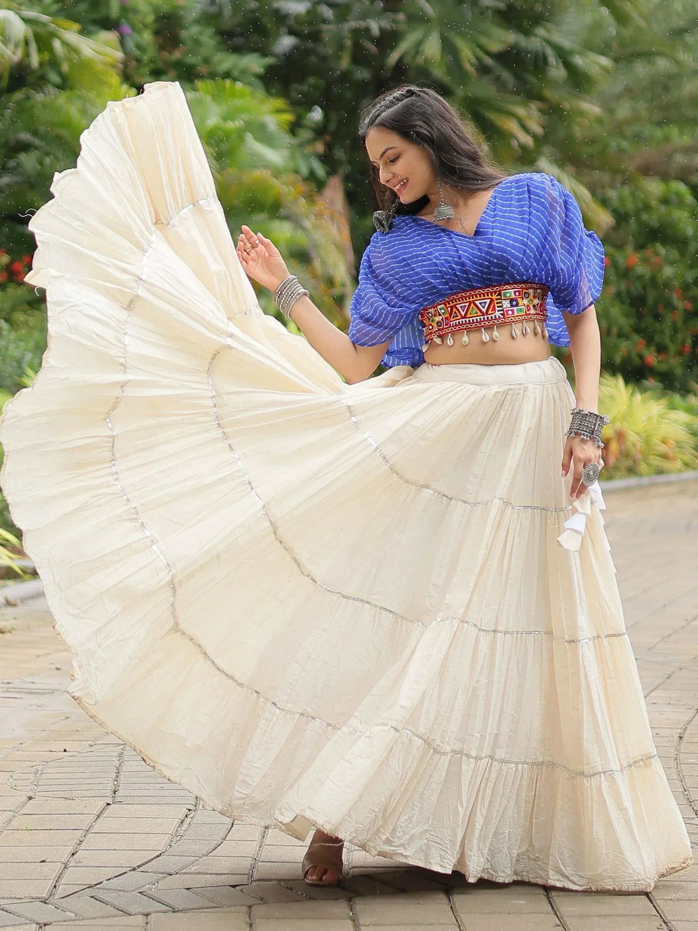 Woman twirling in cream pleated skirt with blue striped blouse, ethnic Indian wear for festive occasions
