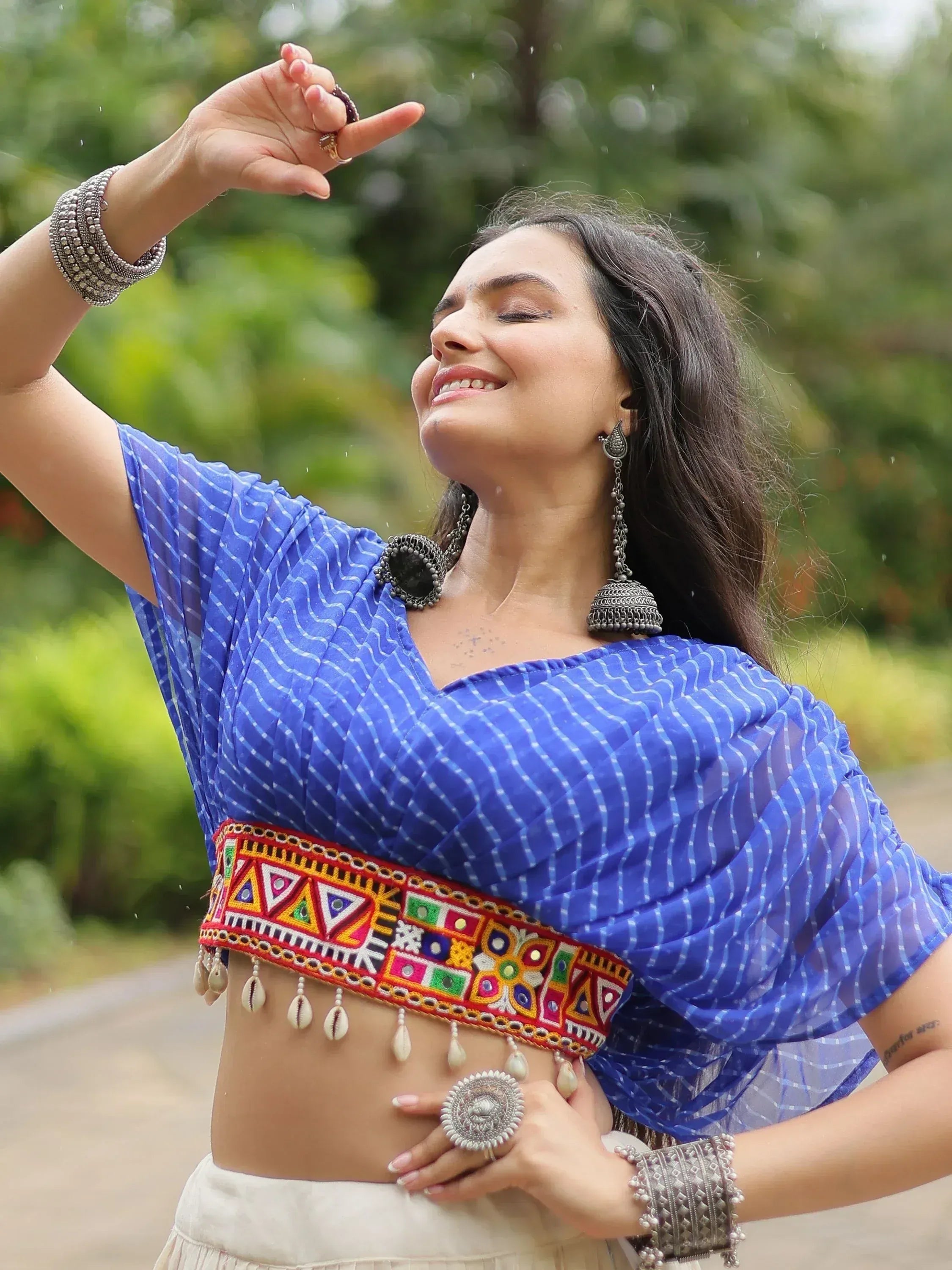 Woman in blue printed ethnic top with colorful embroidered belt and silver jewelry, dancing outdoors