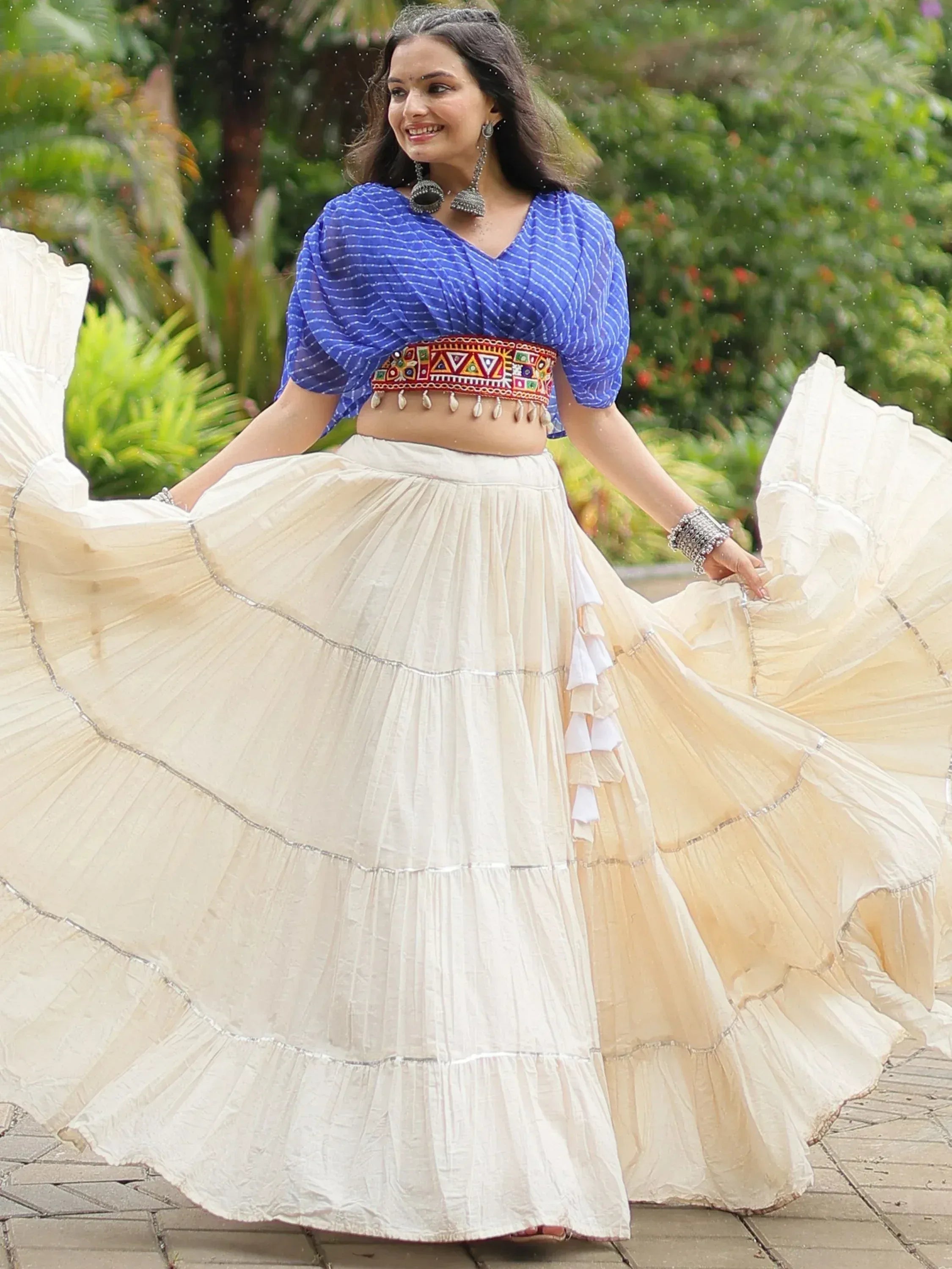 Woman in blue printed crop top and cream tiered skirt, twirling outdoors in ethnic Indian wear