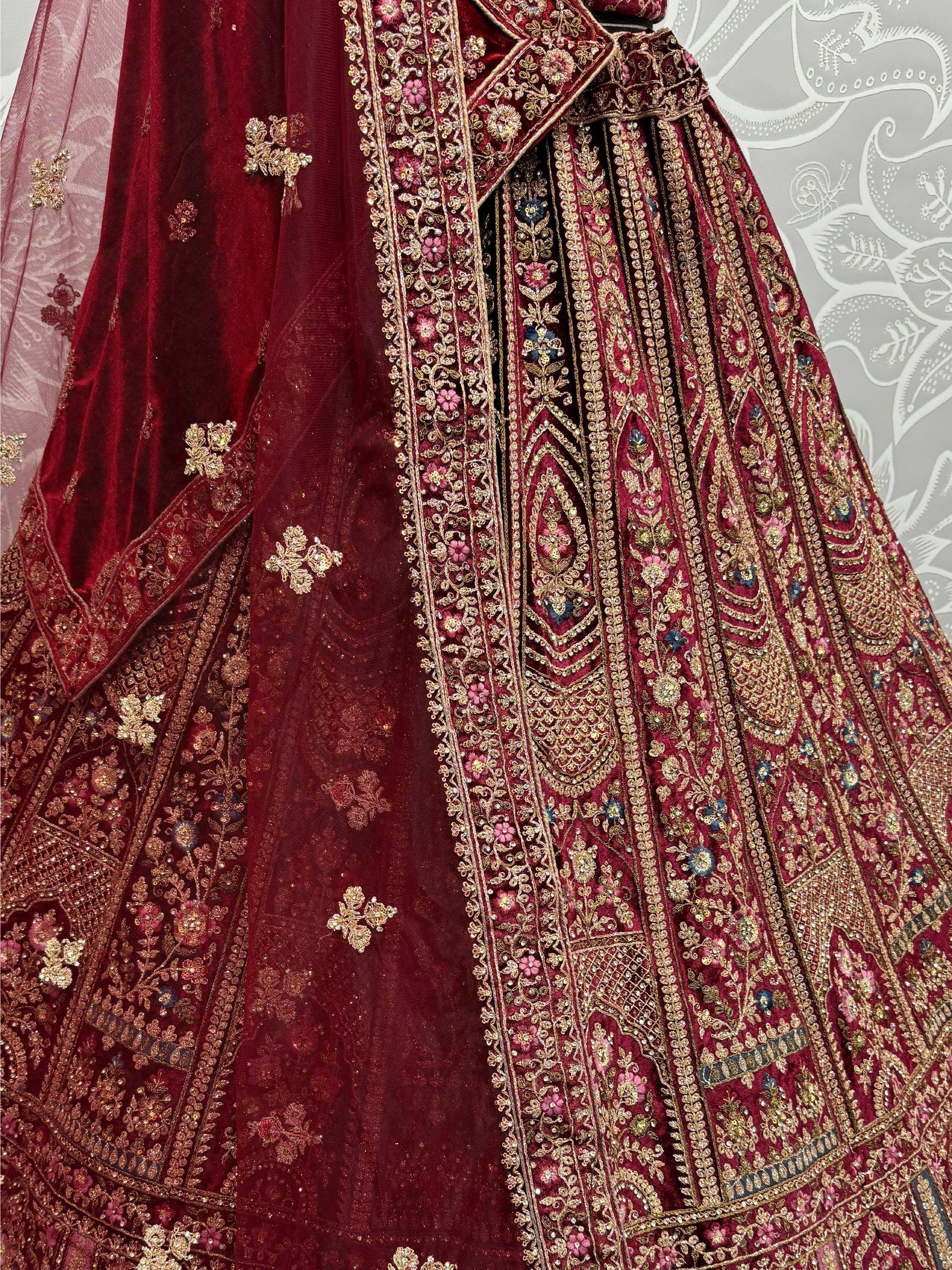 Luxury maroon velvet lehenga choli with intricate gold embroidery and floral motifs, perfect for Indian weddings.