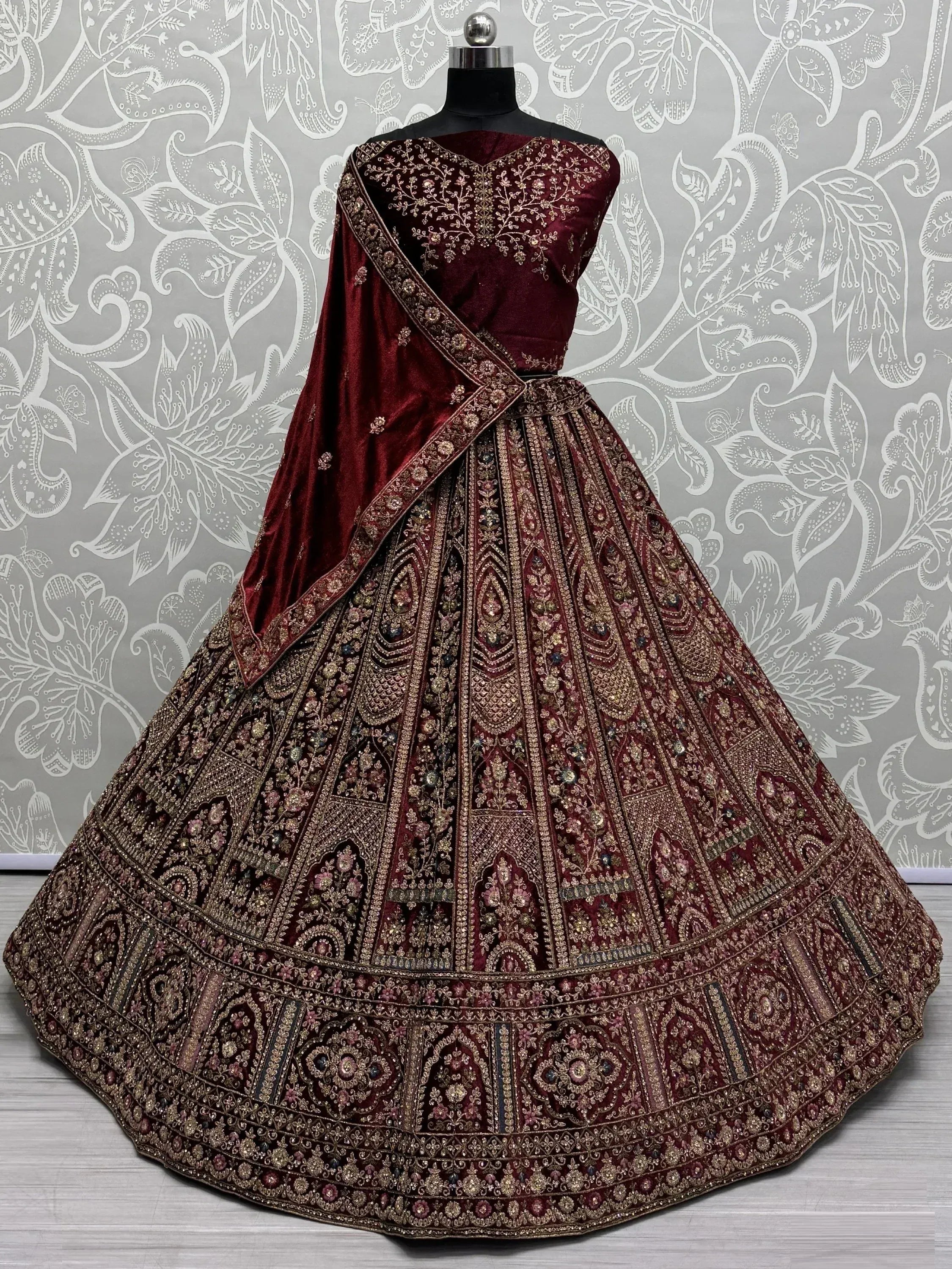 Maroon velvet designer lehenga choli with heavy gold embroidery and floral motifs, perfect for weddings.