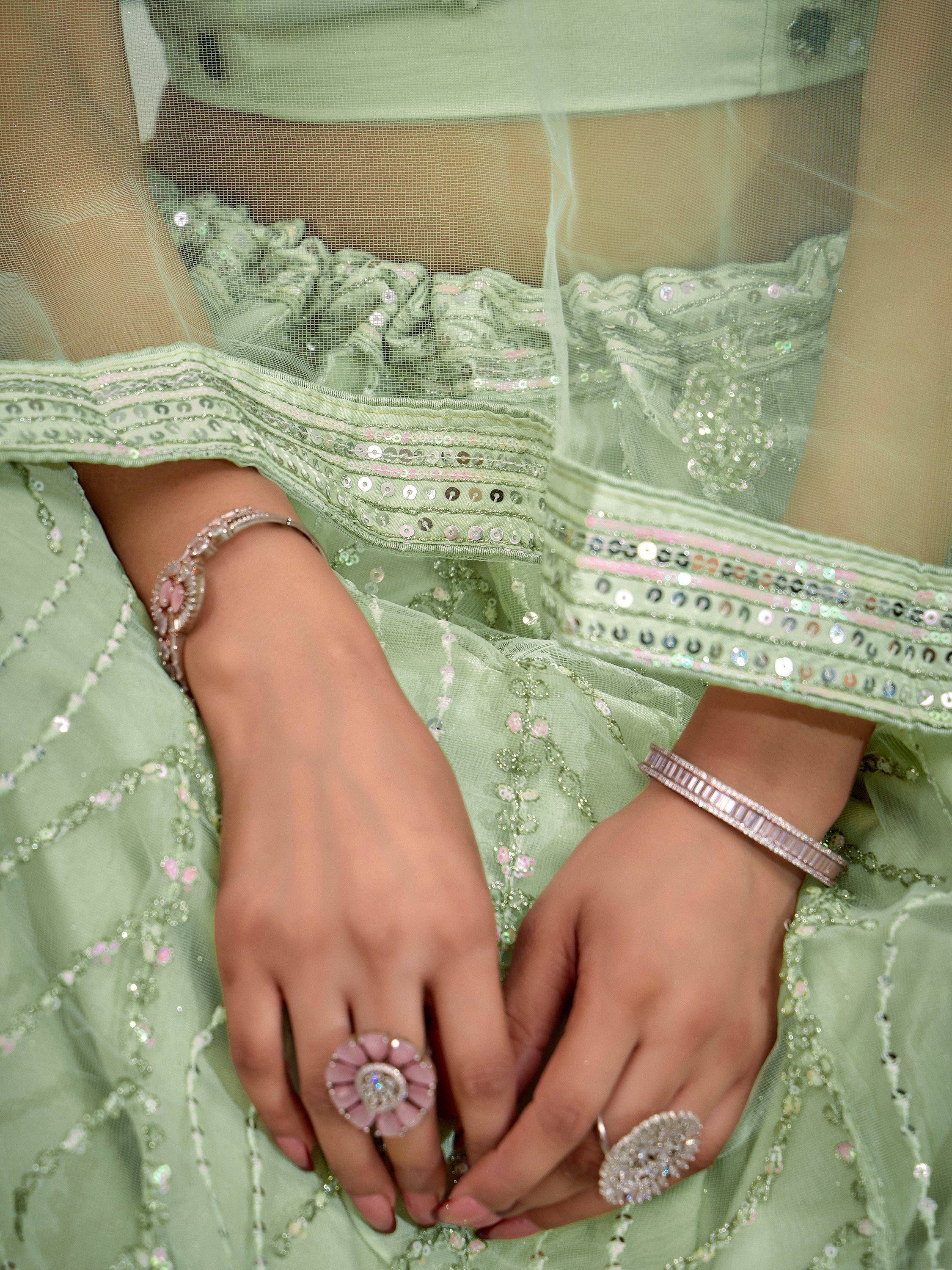 Mint green ethnic gown with sequin embroidery, paired with floral rings and diamond bracelets for festive wear