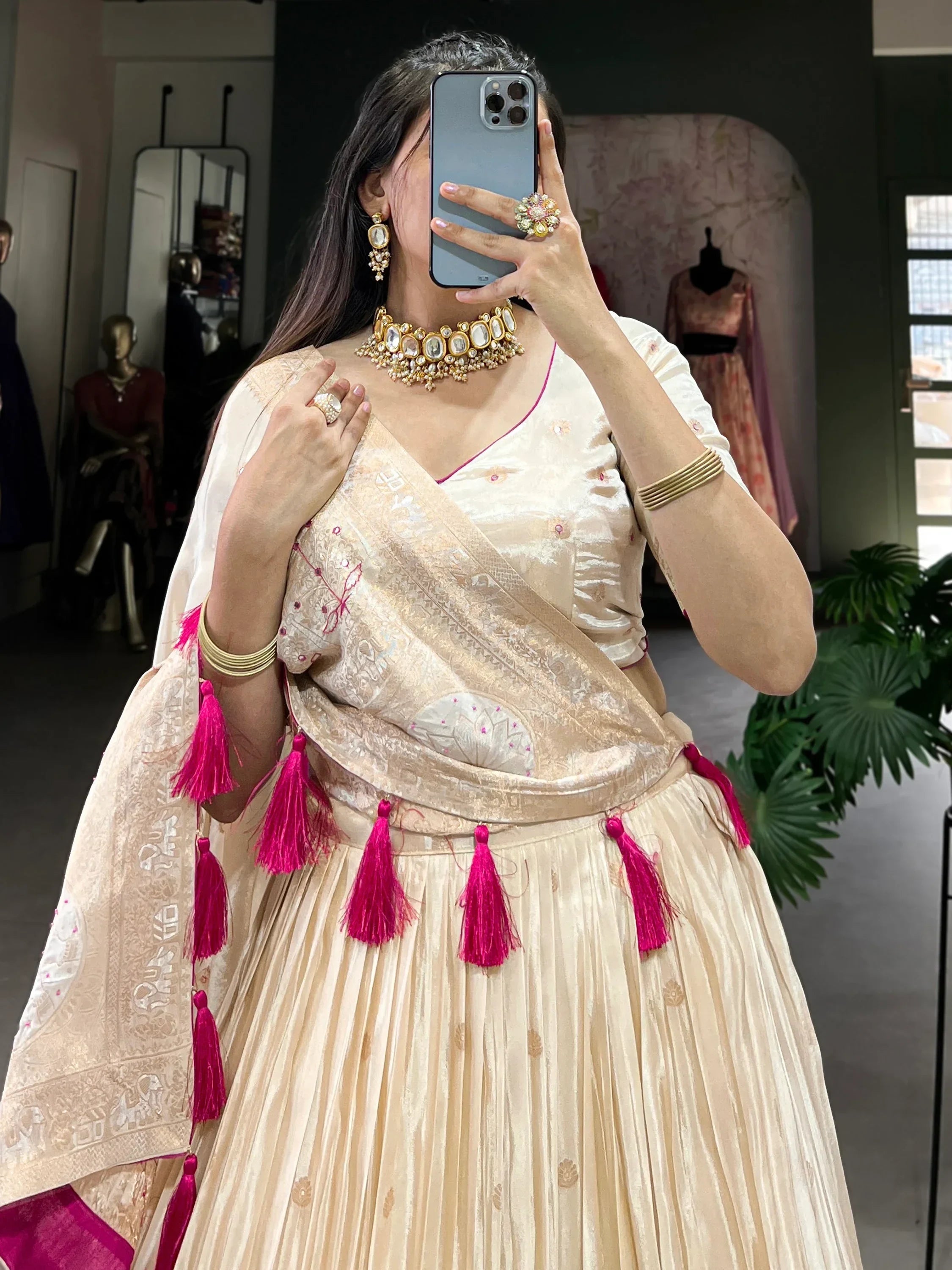 Cream designer lehenga choli with pink tassels and gold jewelry, perfect for Indian ethnic wear