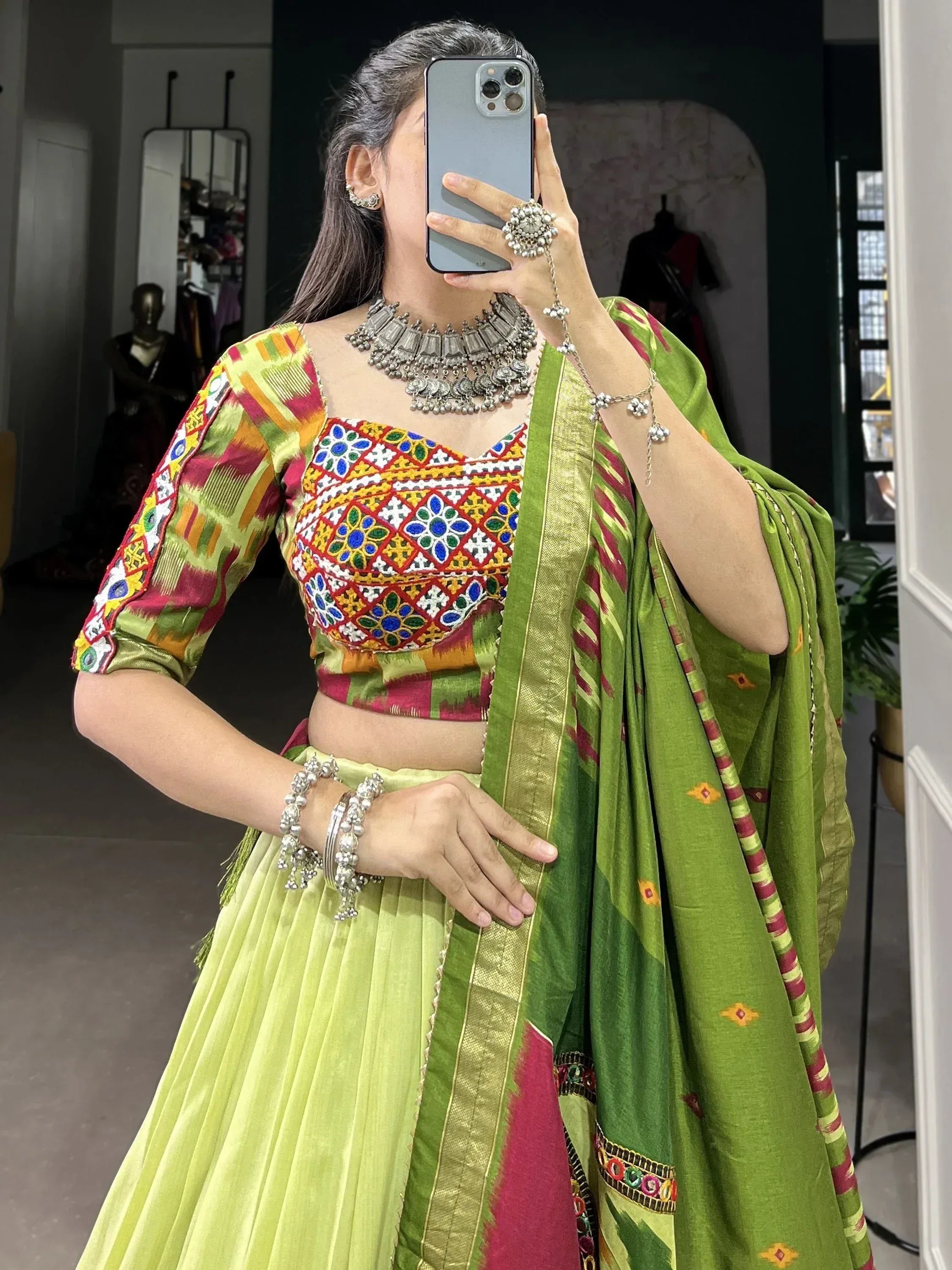 Vibrant green and multicolor embroidered lehenga choli with mirror work, paired with silver jewelry for festive Indian wear.