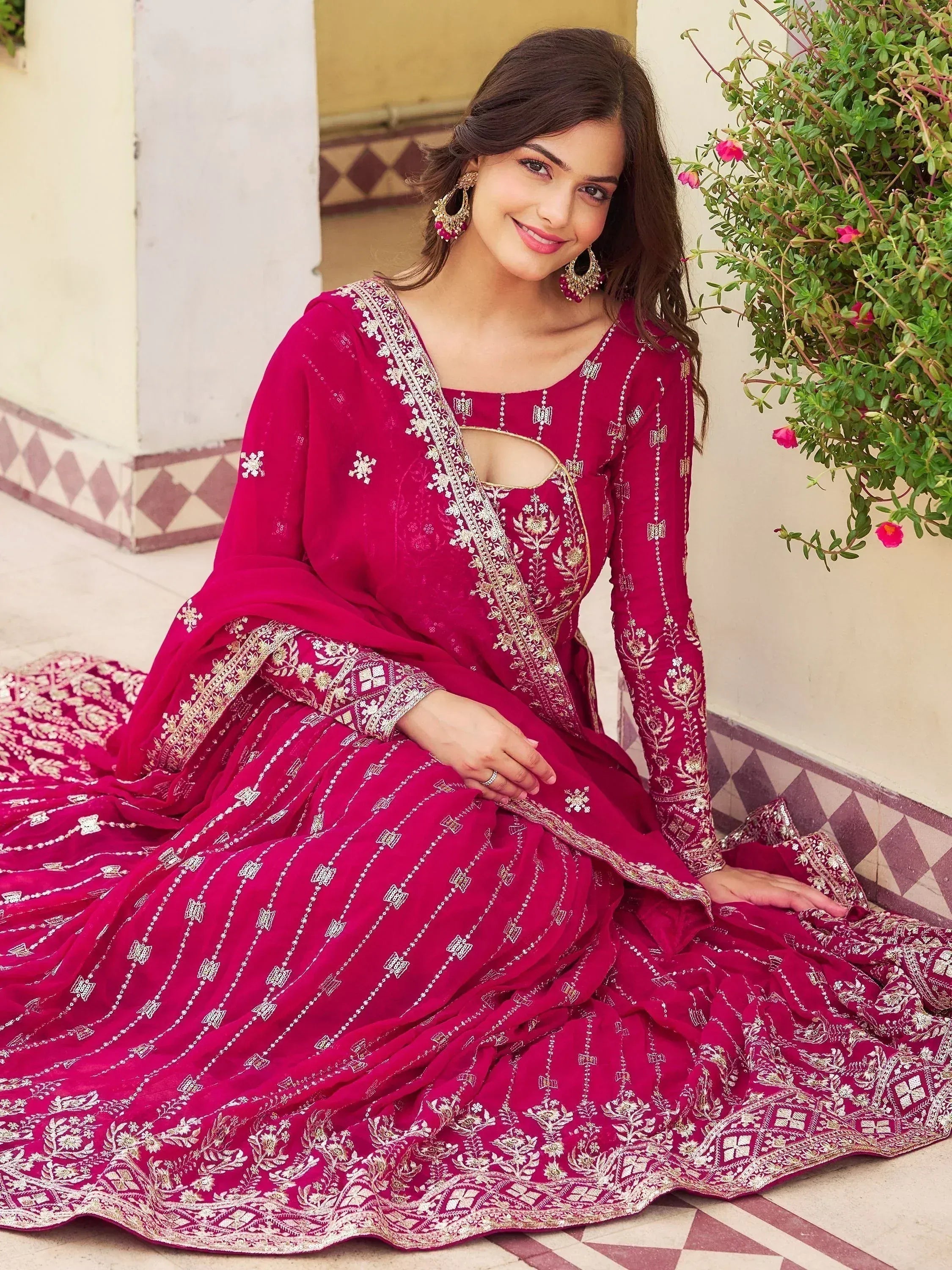 Woman in elegant magenta ethnic gown with gold embroidery, perfect for Indian weddings or festive occasions.