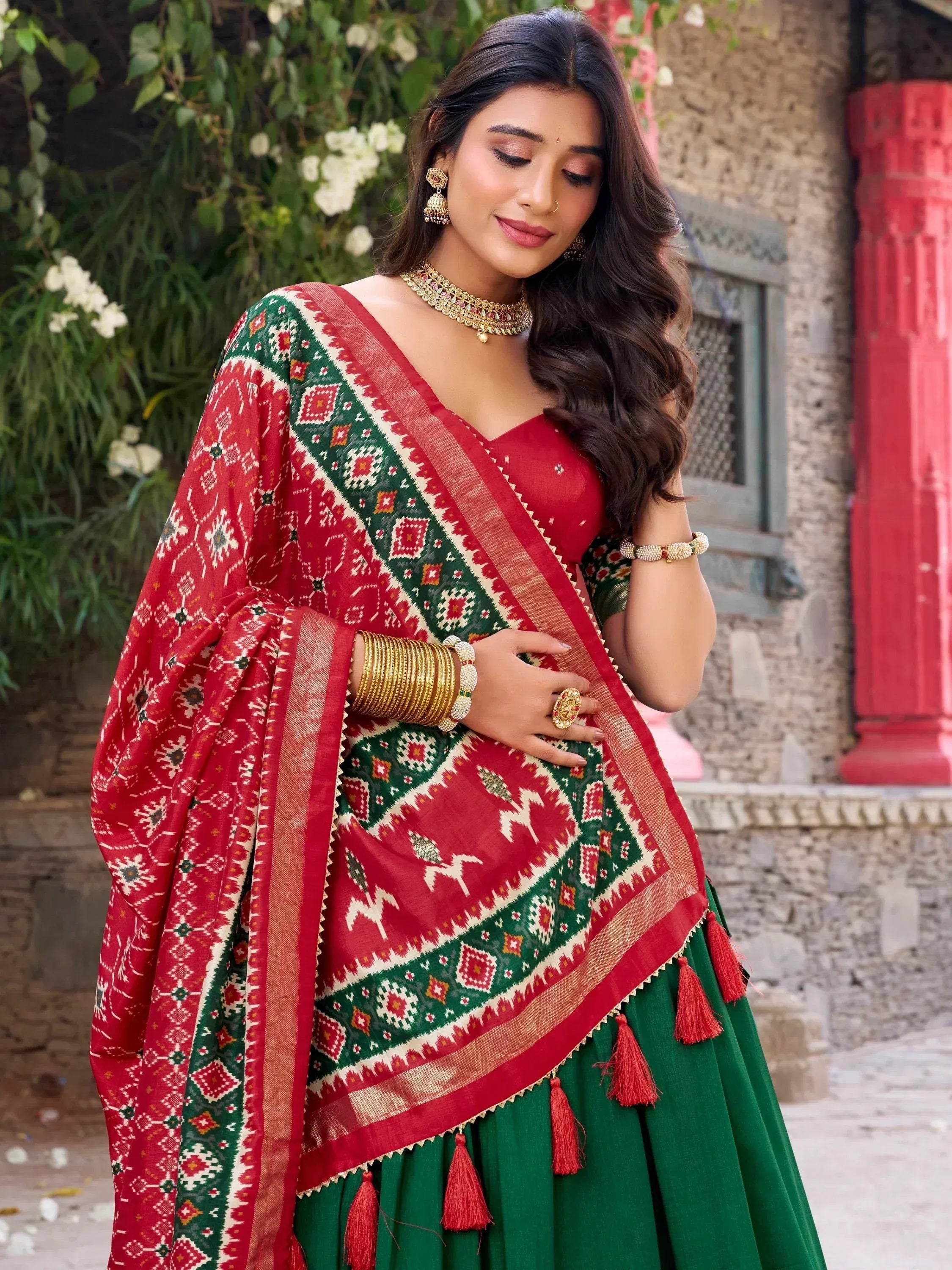 Red and green ethnic saree with geometric print, tassels, and gold jewelry for festive occasions