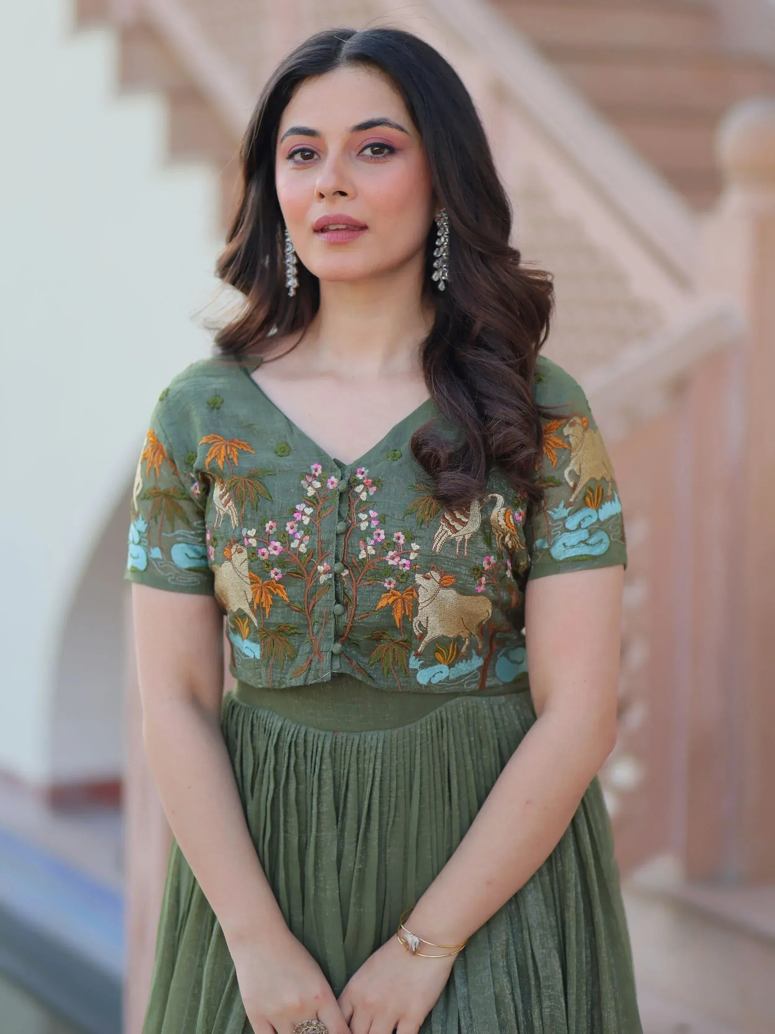Woman in olive green embroidered ethnic gown with floral and animal motifs, perfect for Indian occasions.
