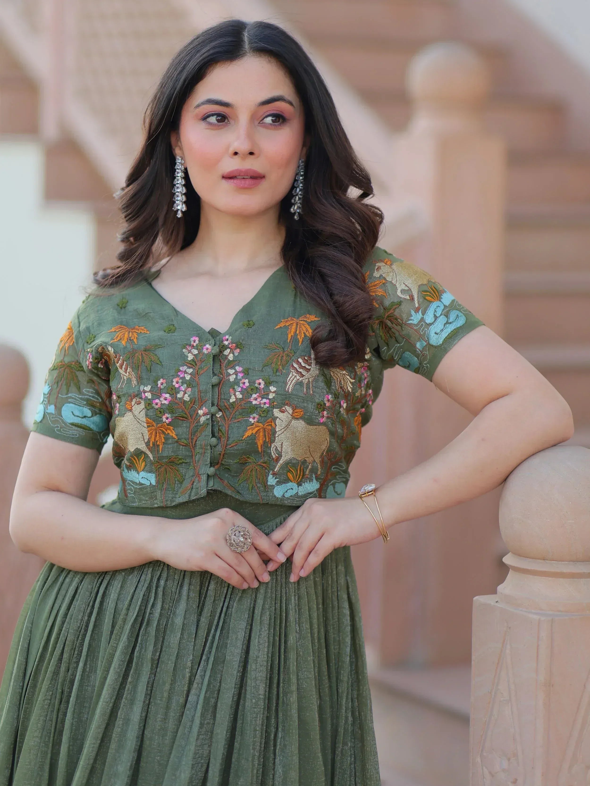 Woman in olive green embroidered ethnic gown with floral and animal motifs, perfect for Indian occasions.