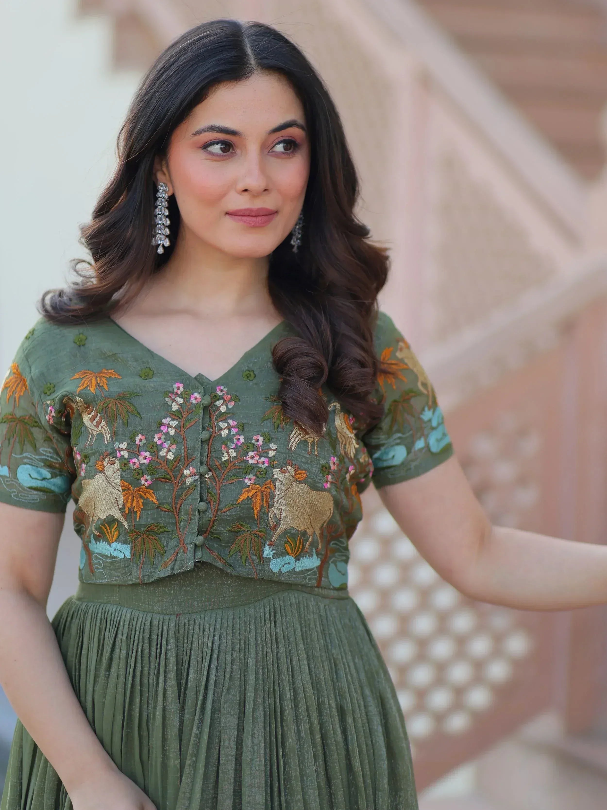 Woman in olive green embroidered ethnic gown with floral and animal motifs, perfect for Indian occasions.