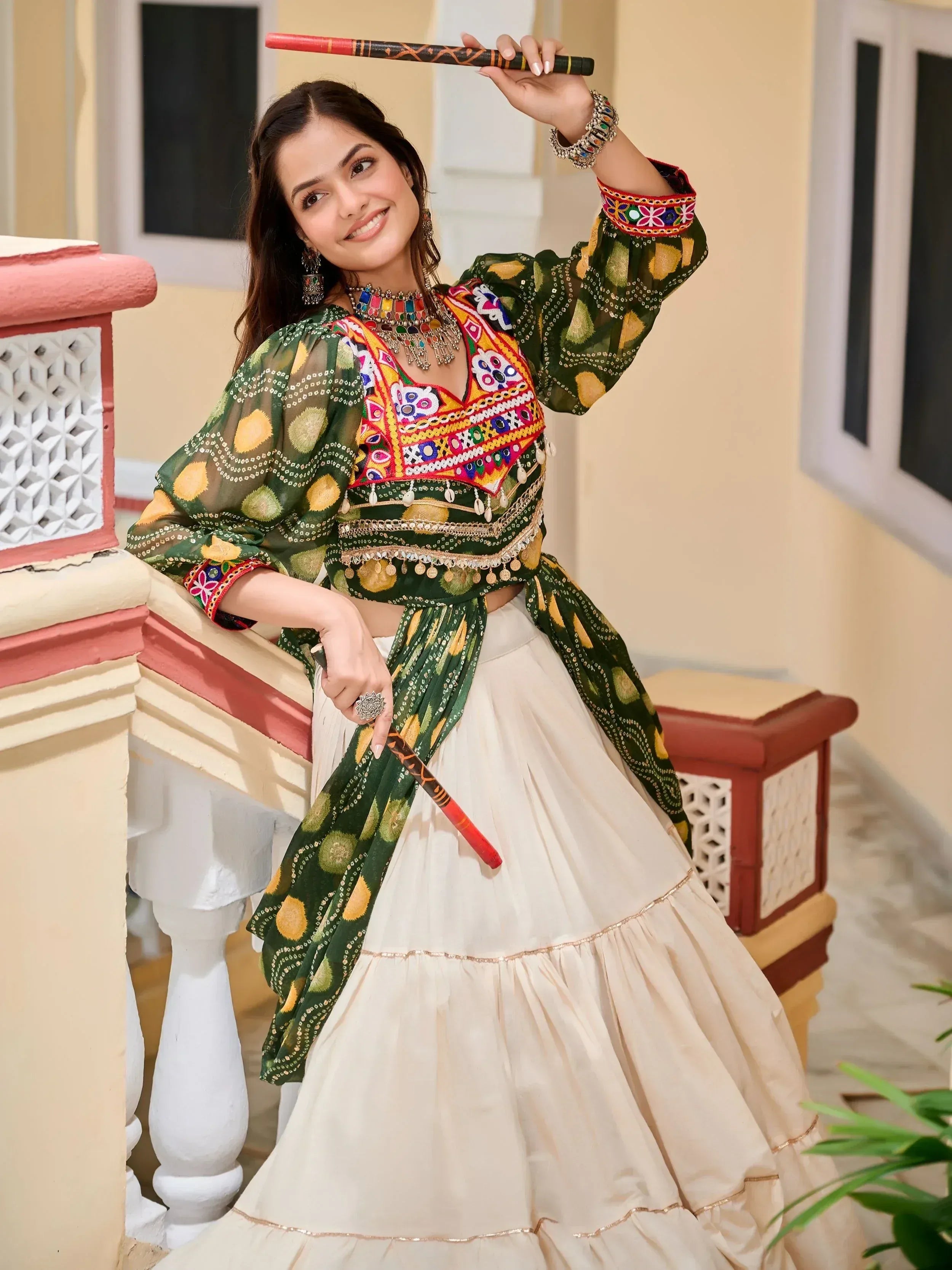 Woman in green embroidered Indian ethnic wear with mirror work, holding dandiya sticks, perfect for festive occasions
