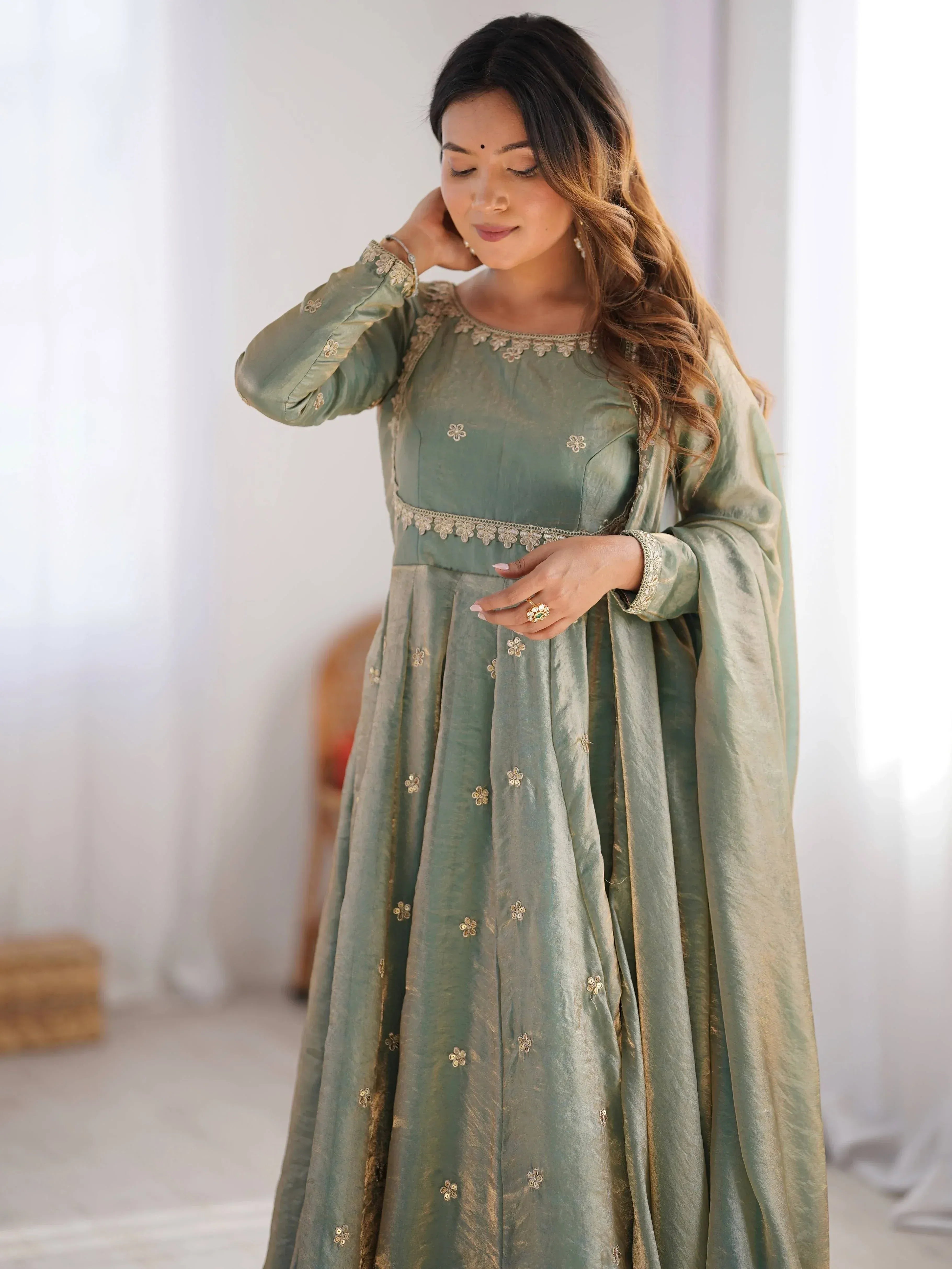 Woman wearing a pastel green embroidered ethnic gown with dupatta indoors