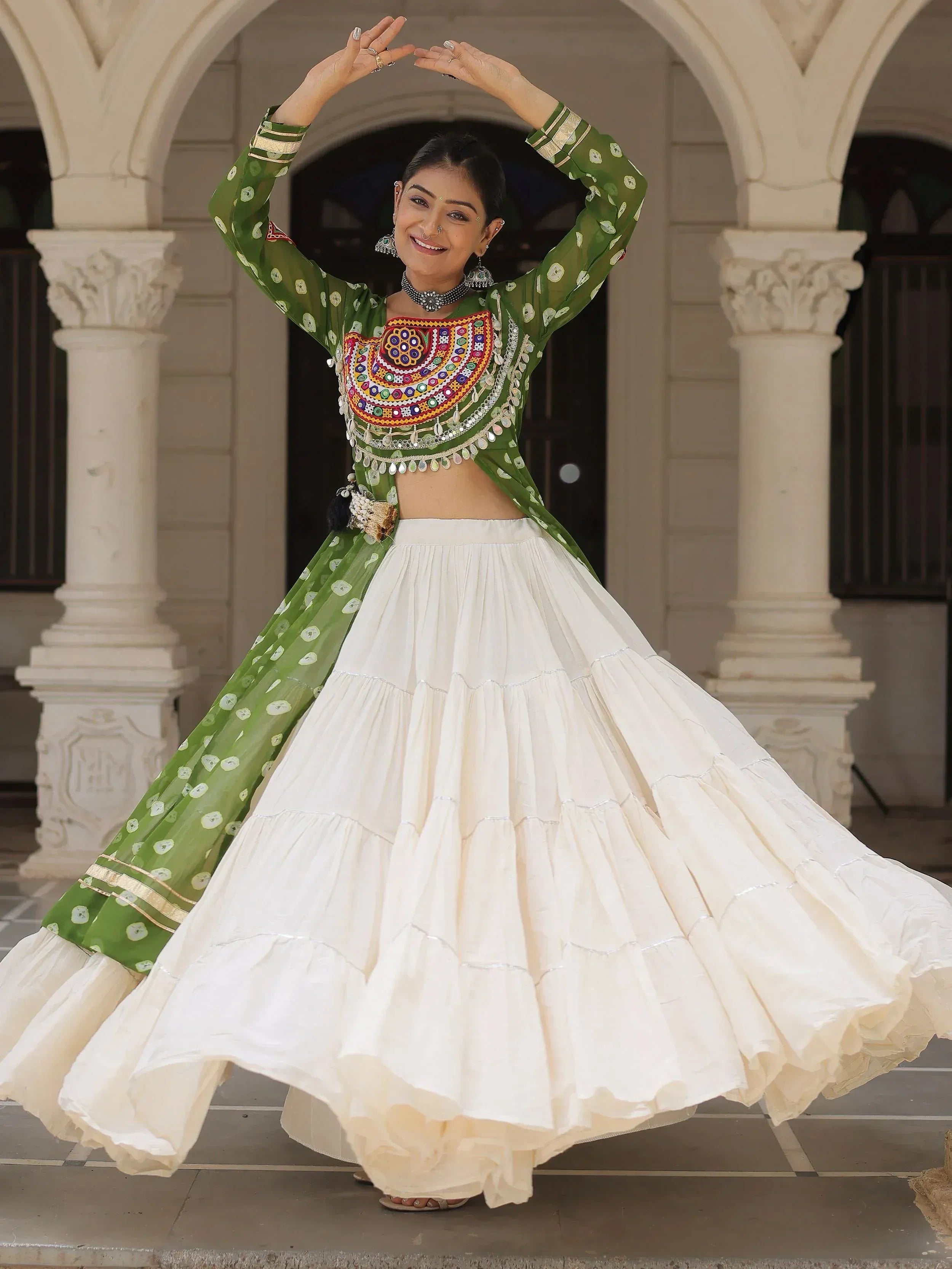 Woman in green embroidered choli and white lehenga dancing under arches, Indian ethnic wear