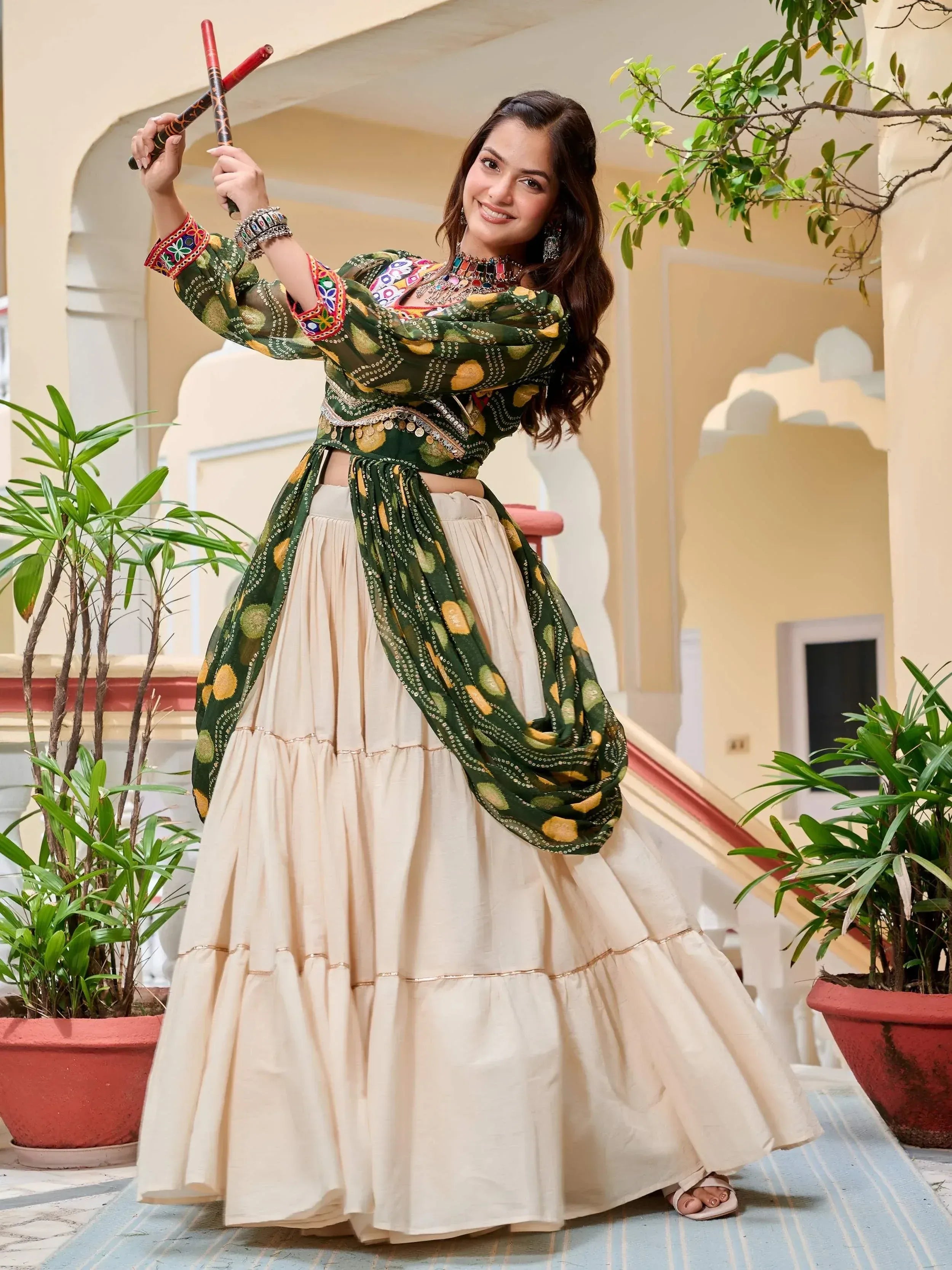 Woman in green embroidered crop top and cream tiered skirt with dandiya sticks, Indian ethnic wear