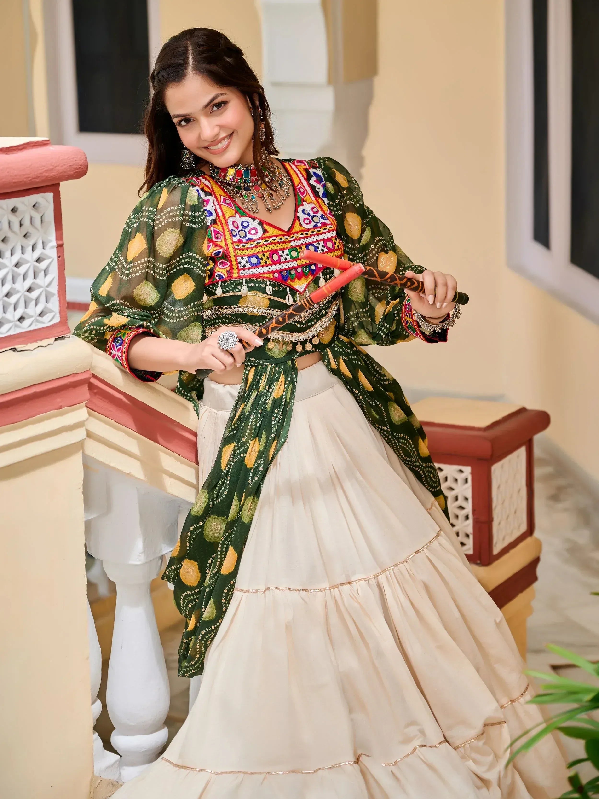 Woman in vibrant green embroidered top with white tiered skirt, holding traditional dandiya sticks, festive Indian ethnic wear