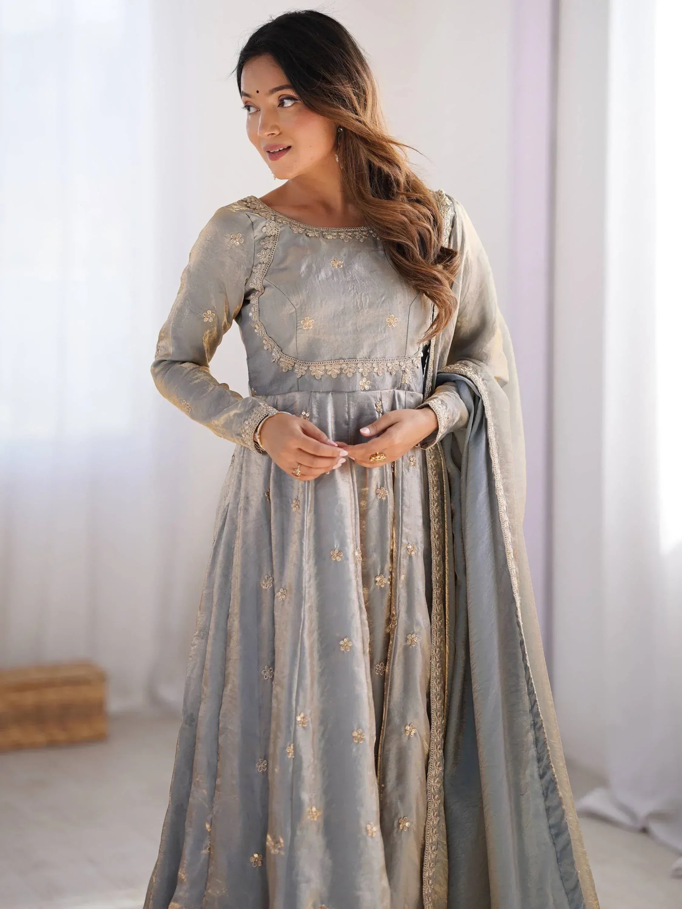 Woman in grey embroidered ethnic gown with long sleeves and dupatta, standing indoors