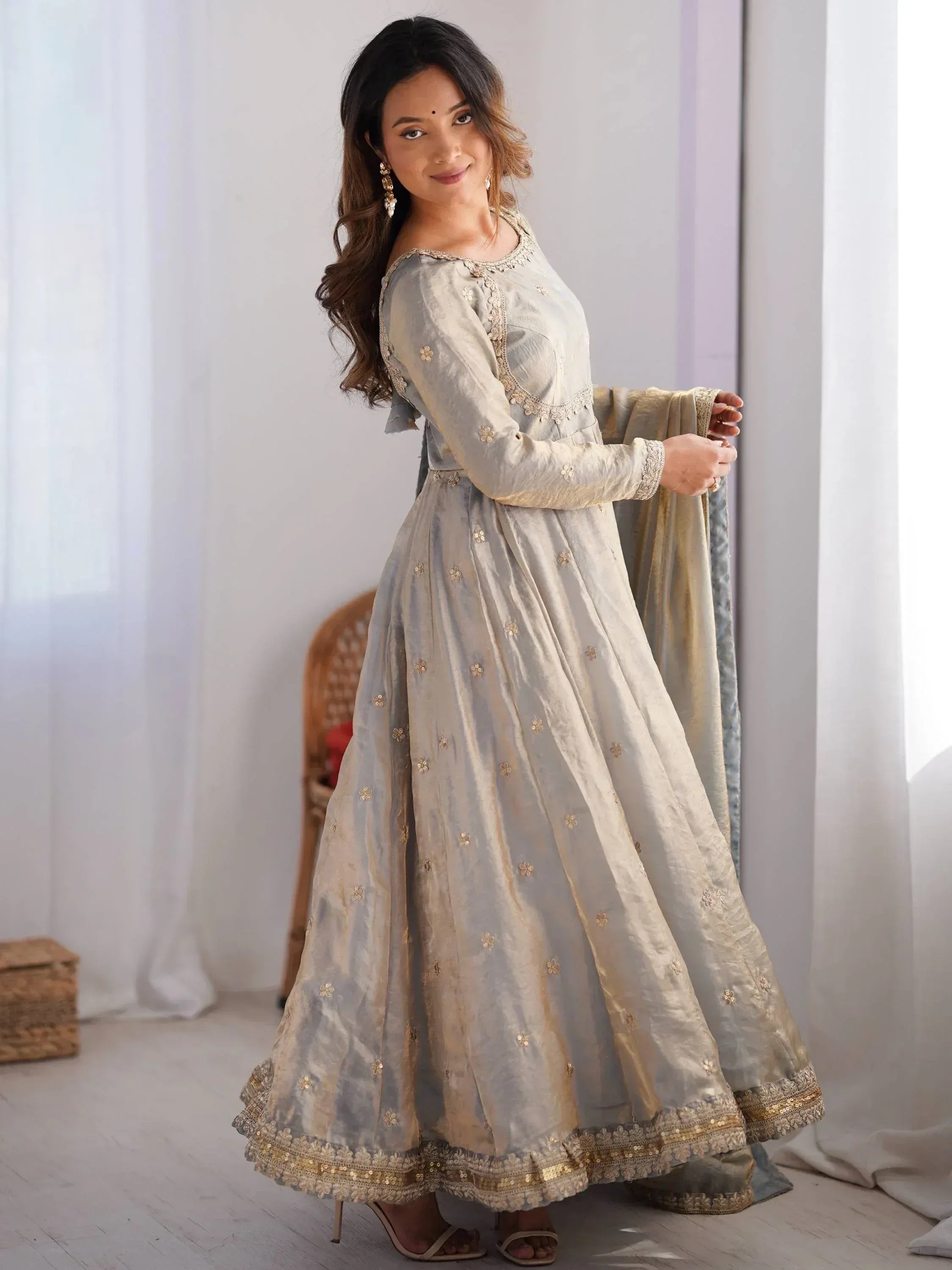 Woman in light grey ethnic gown with gold embroidery and dupatta in a bright room