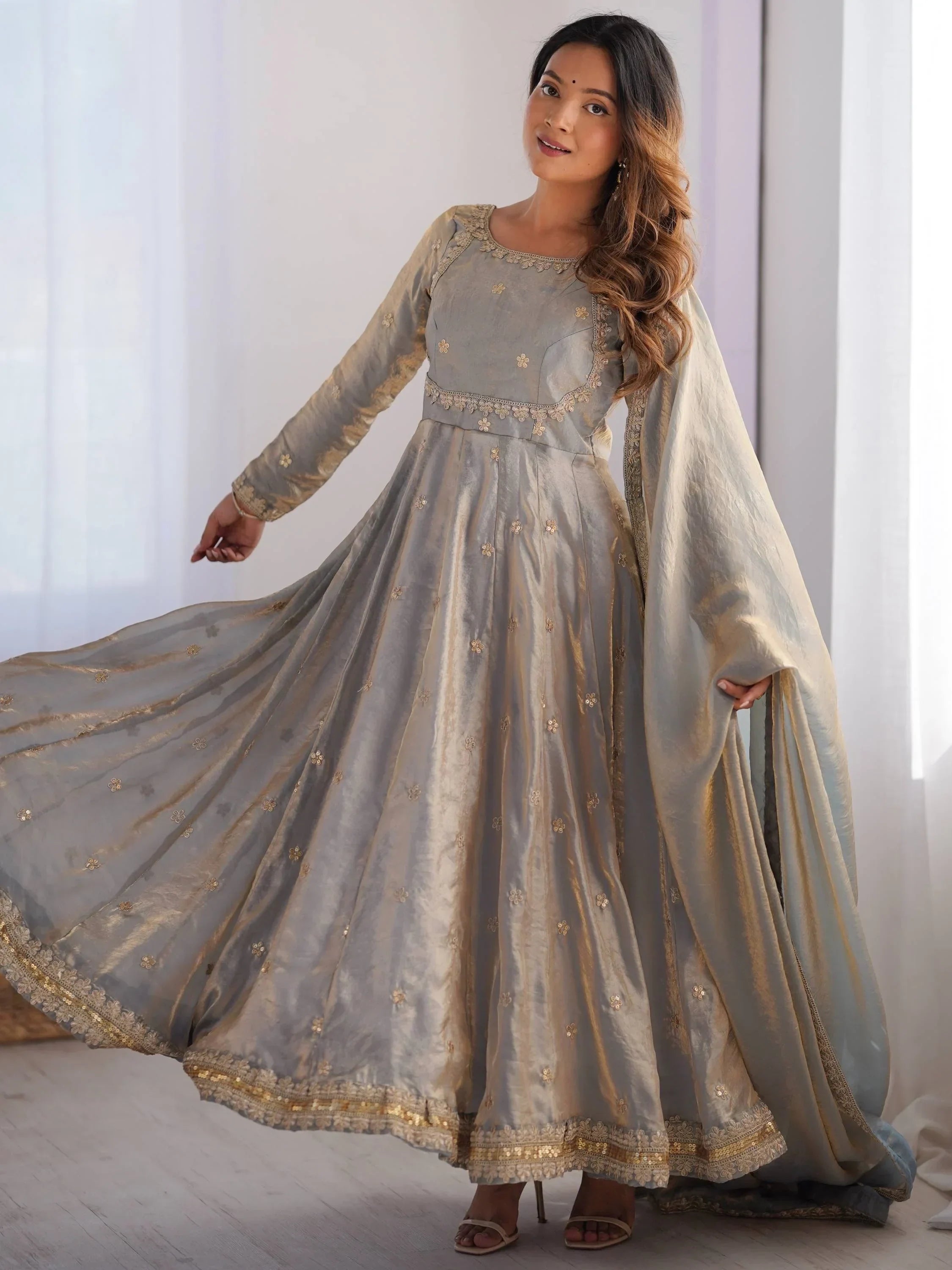 Woman in grey embroidered Anarkali gown with dupatta, long sleeves, and gold detailing