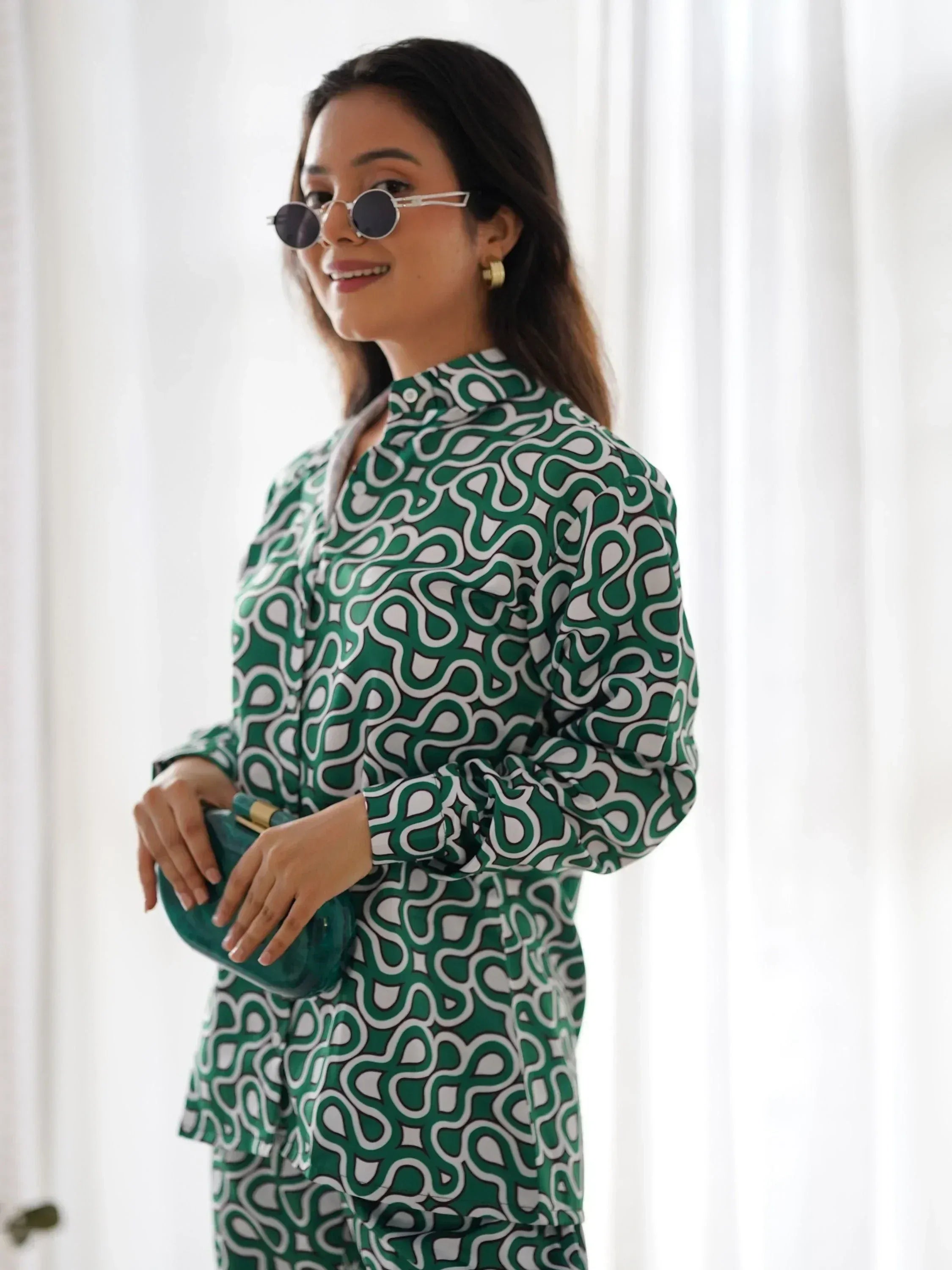 Woman wearing green and white printed kurta set, holding teal clutch, and sunglasses