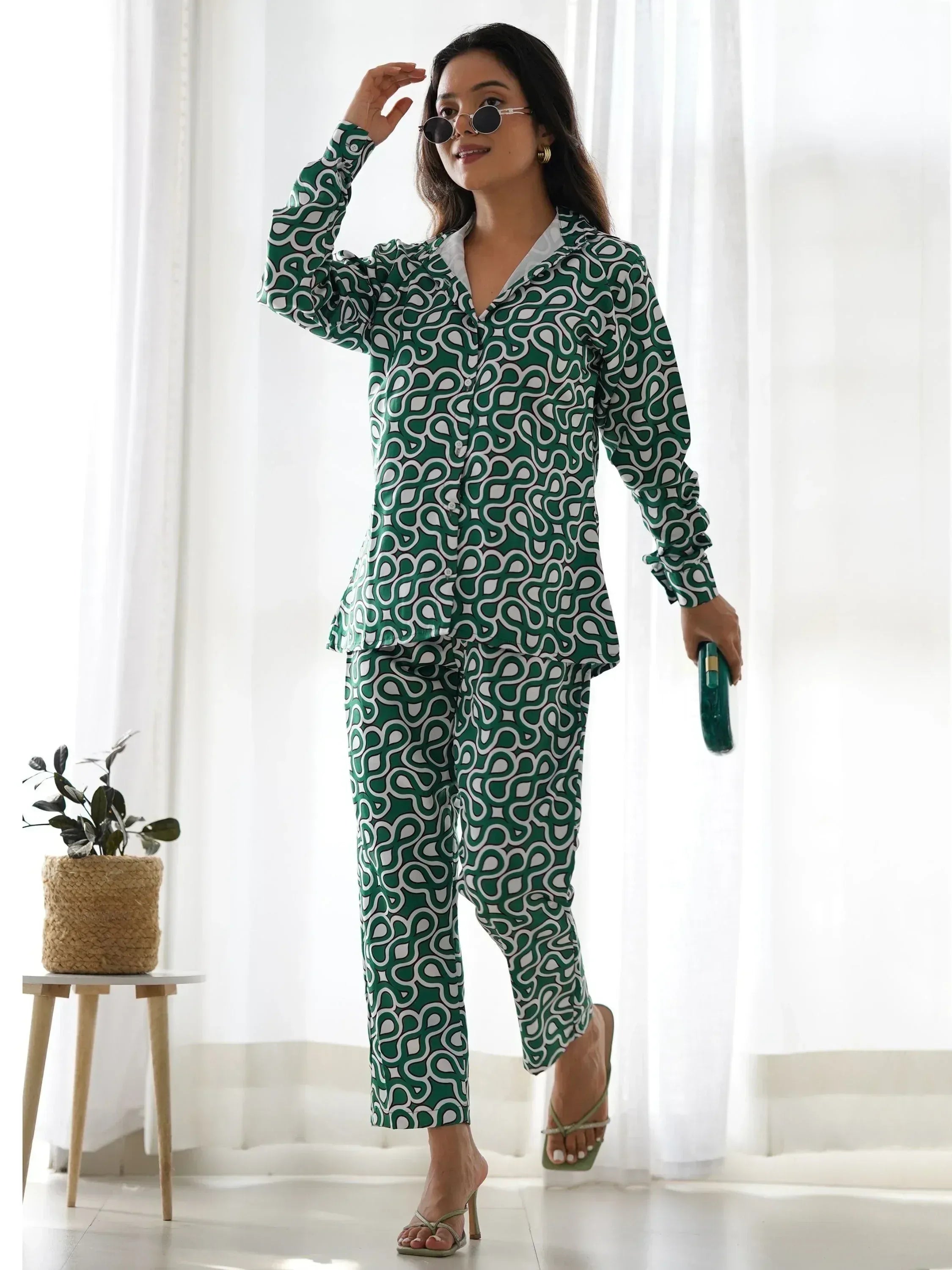 Woman in green and white printed kurta set with pants, holding clutch, posing indoors