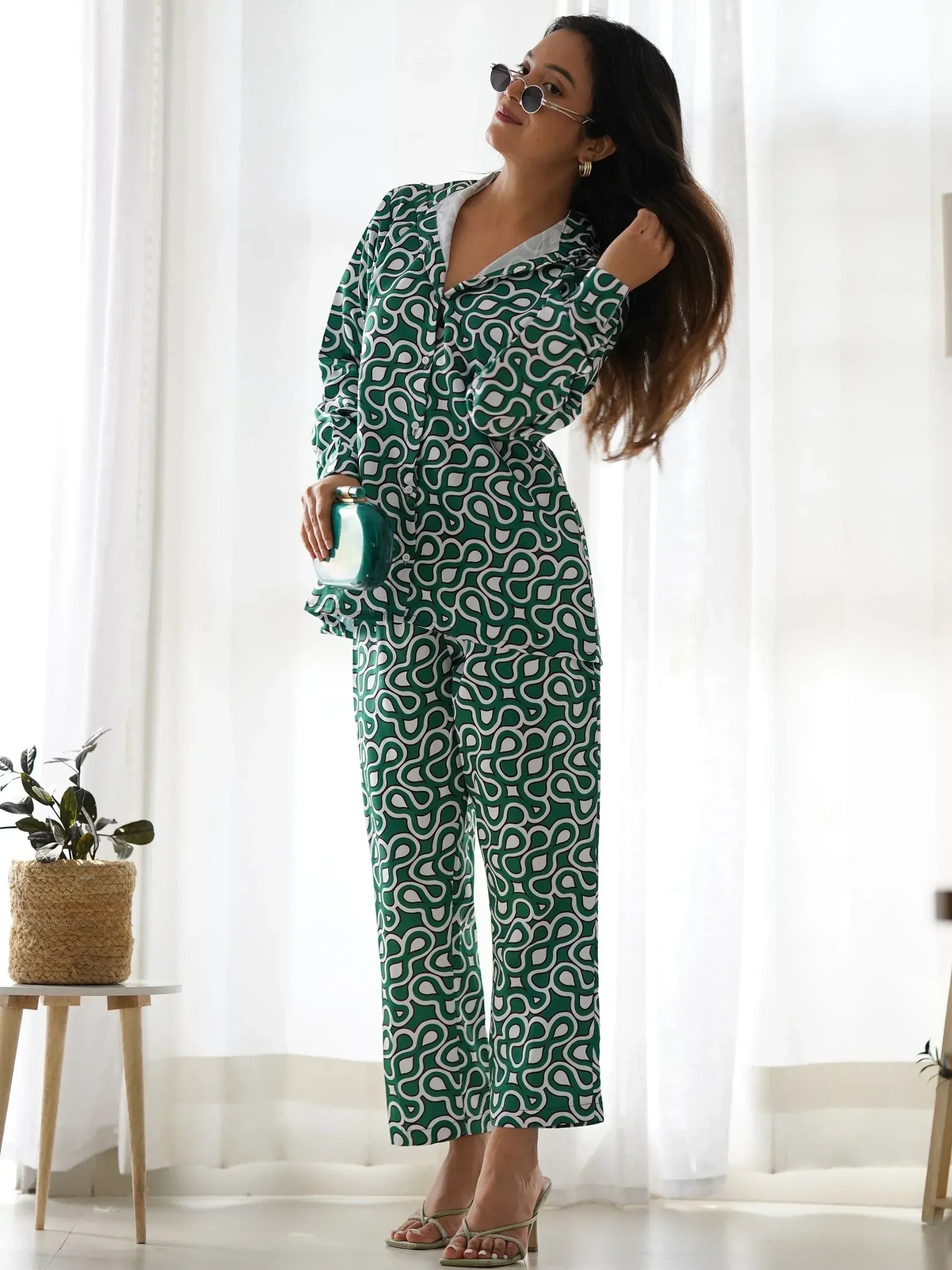 Woman wearing green geometric print pantsuit with clutch, posing indoors by window
