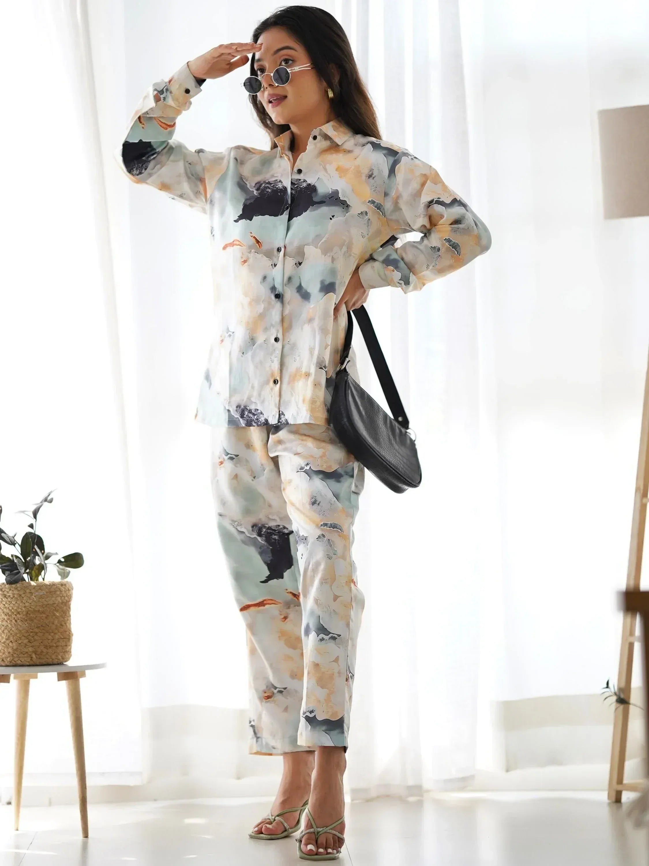 Woman in abstract print ethnic shirt and pants set, stylish casual wear with sunglasses and black bag