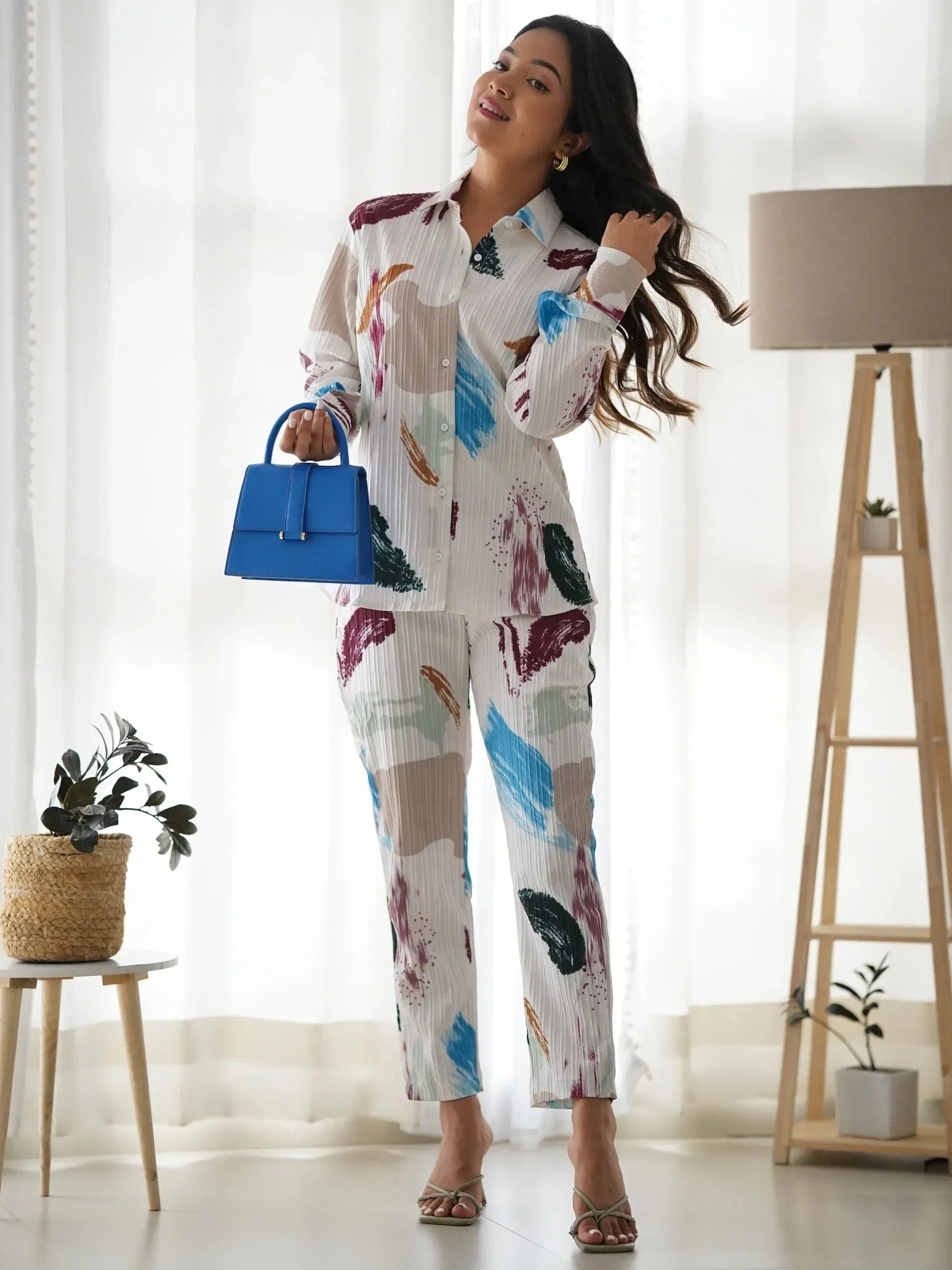 Woman in colorful abstract print pleated shirt and pants set with blue handbag, stylish ethnic wear outfit