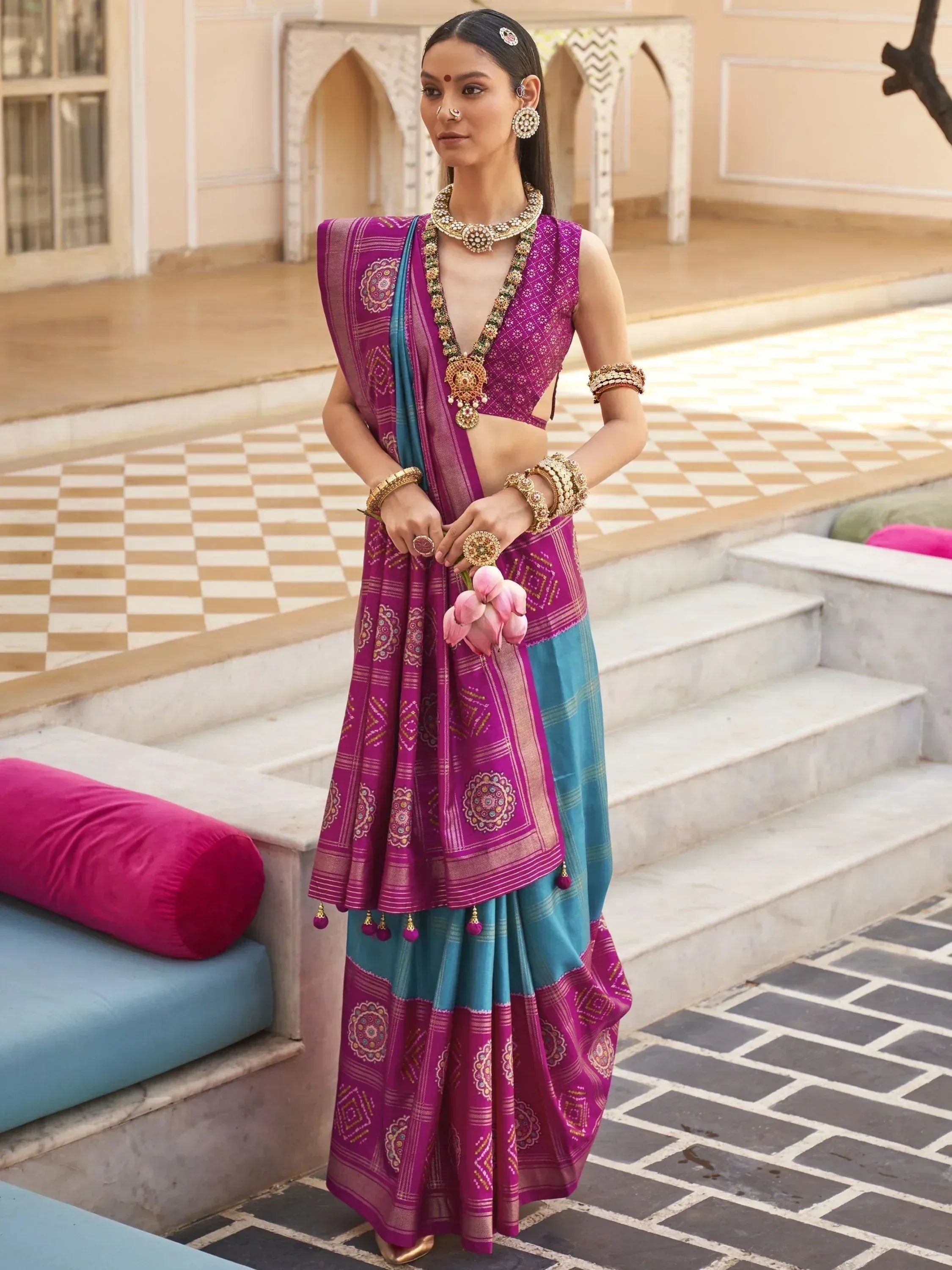 Woman in purple and teal designer lehenga choli with intricate embroidery, traditional jewelry, and lotus flowers