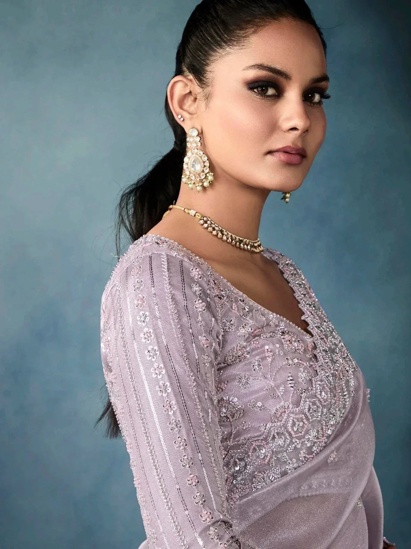 Elegant lavender ethnic gown with intricate embroidery and pearl jewelry, perfect for Indian festive occasions.